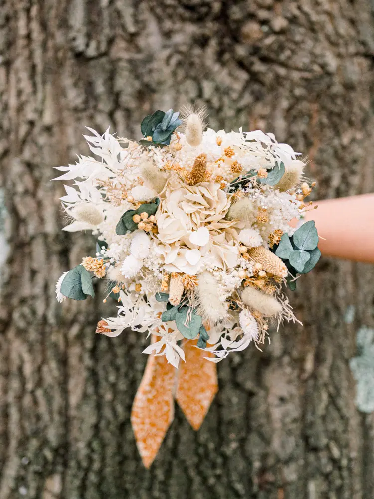 Cream dried-flower bouquet with a mustard ribbon against a tree trunk