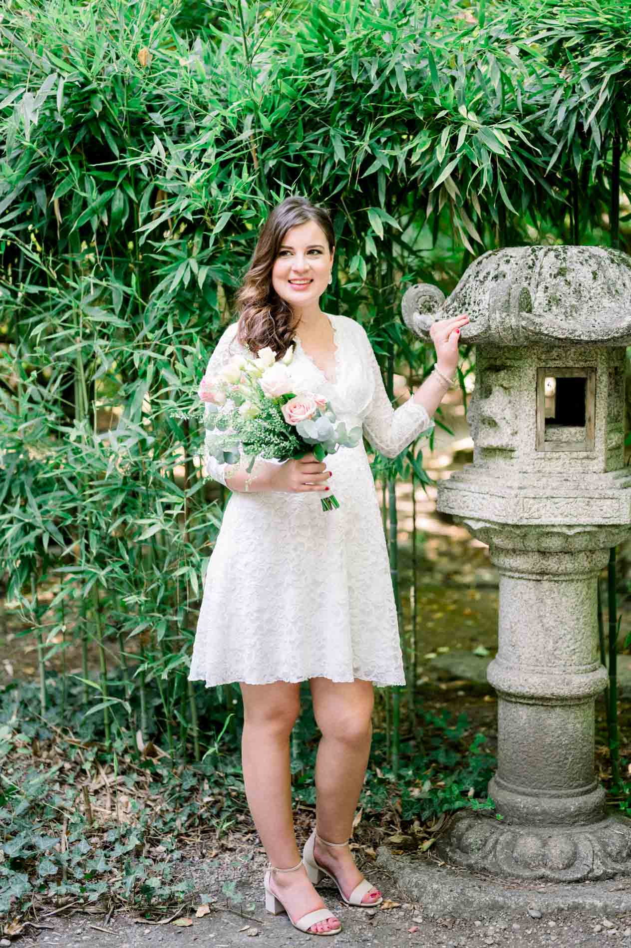 Mother-to-be in a white lace dress beside a stone lantern