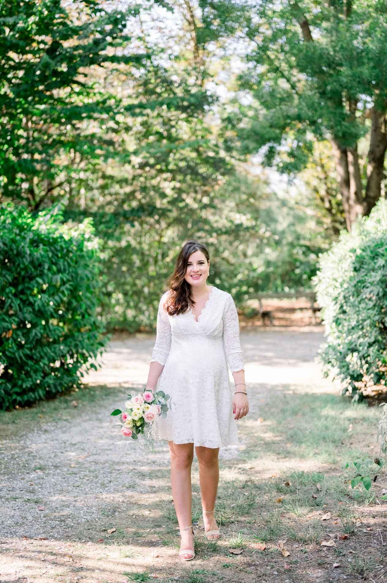 Mother-to-be walking along a shady path, bouquet in hand