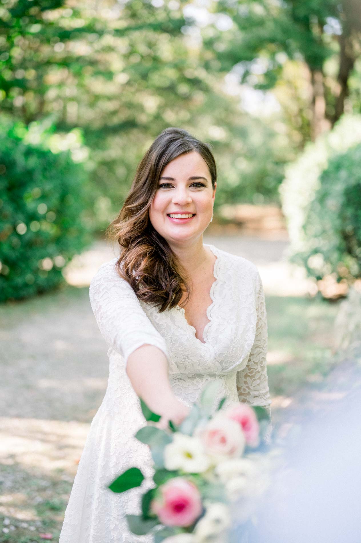 Smiling mother-to-be holding her bouquet out towards the camera on the path