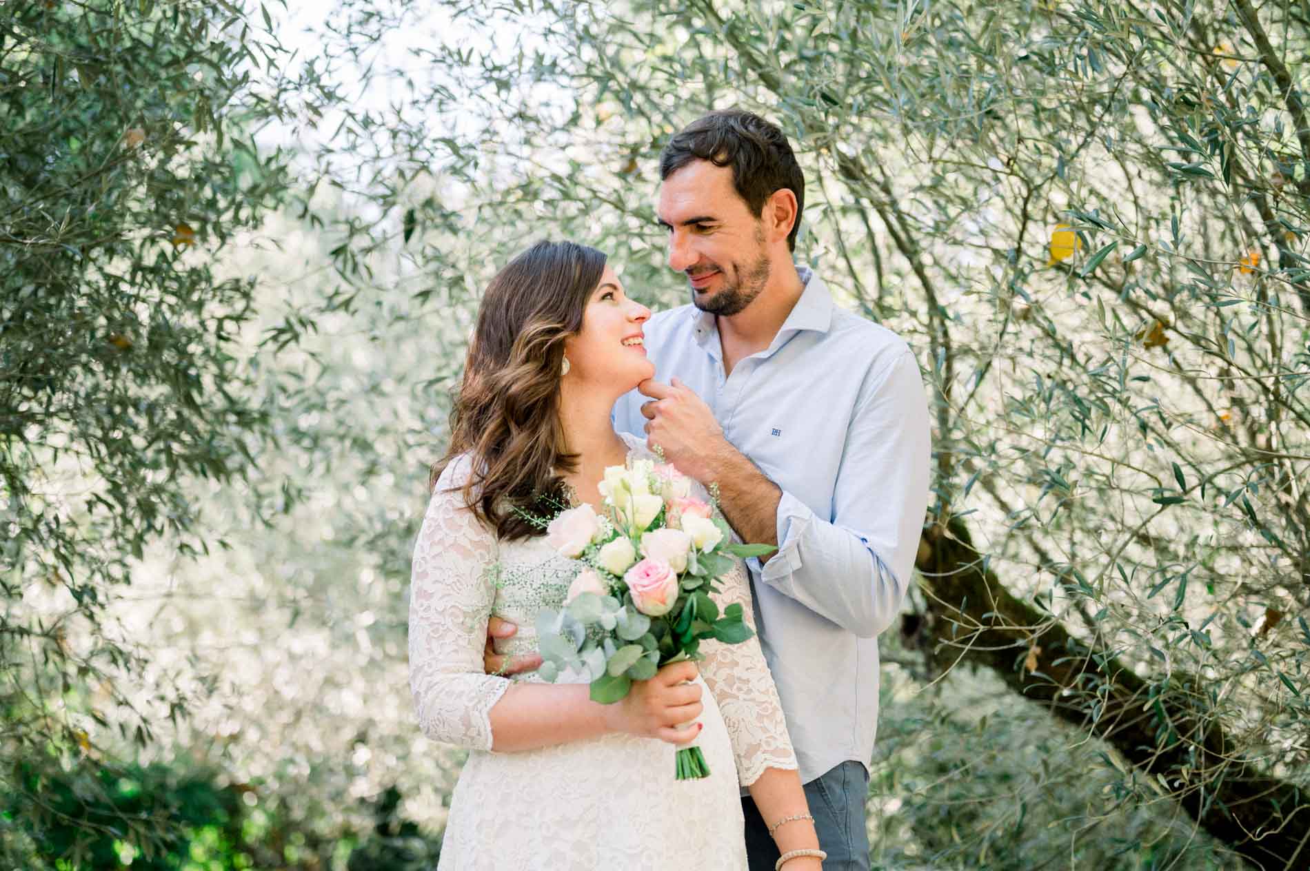Parents-to-be embracing under an olive tree with roses, maternity session at Les Barails