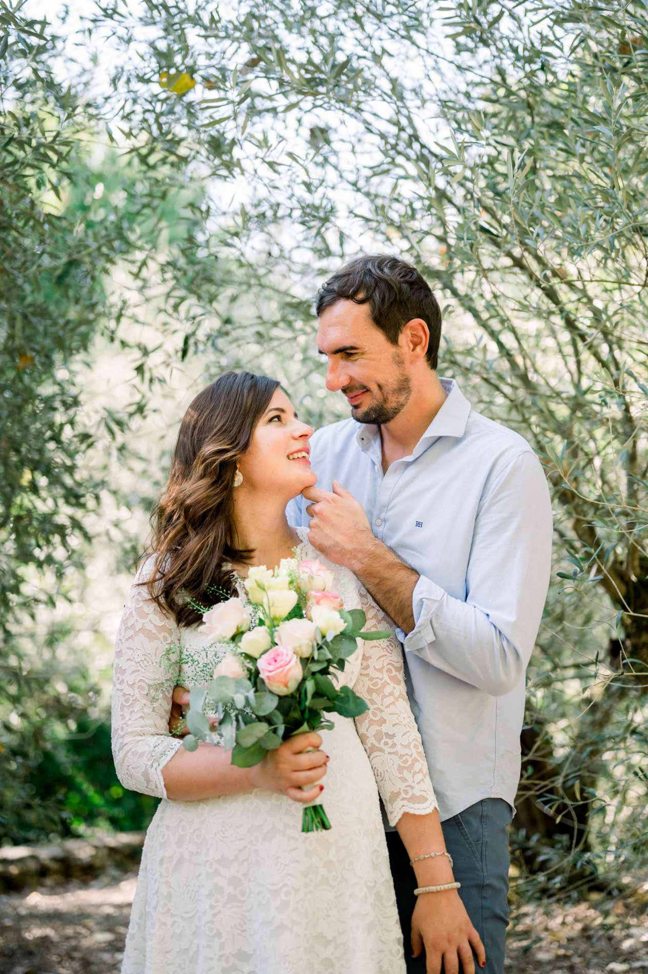 Father-to-be tucking back his pregnant partner's hair under the olive trees