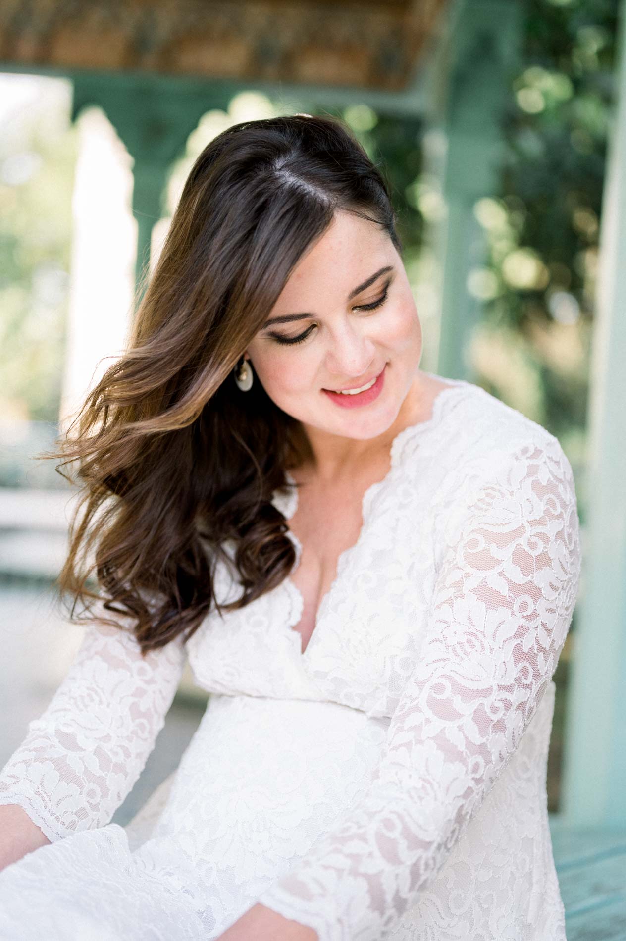 Smiling mother-to-be with lowered eyes under the pavilion, lace dress