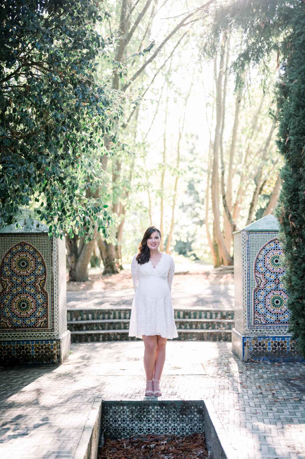 Mother-to-be standing between two mosaic fountains beneath the trees