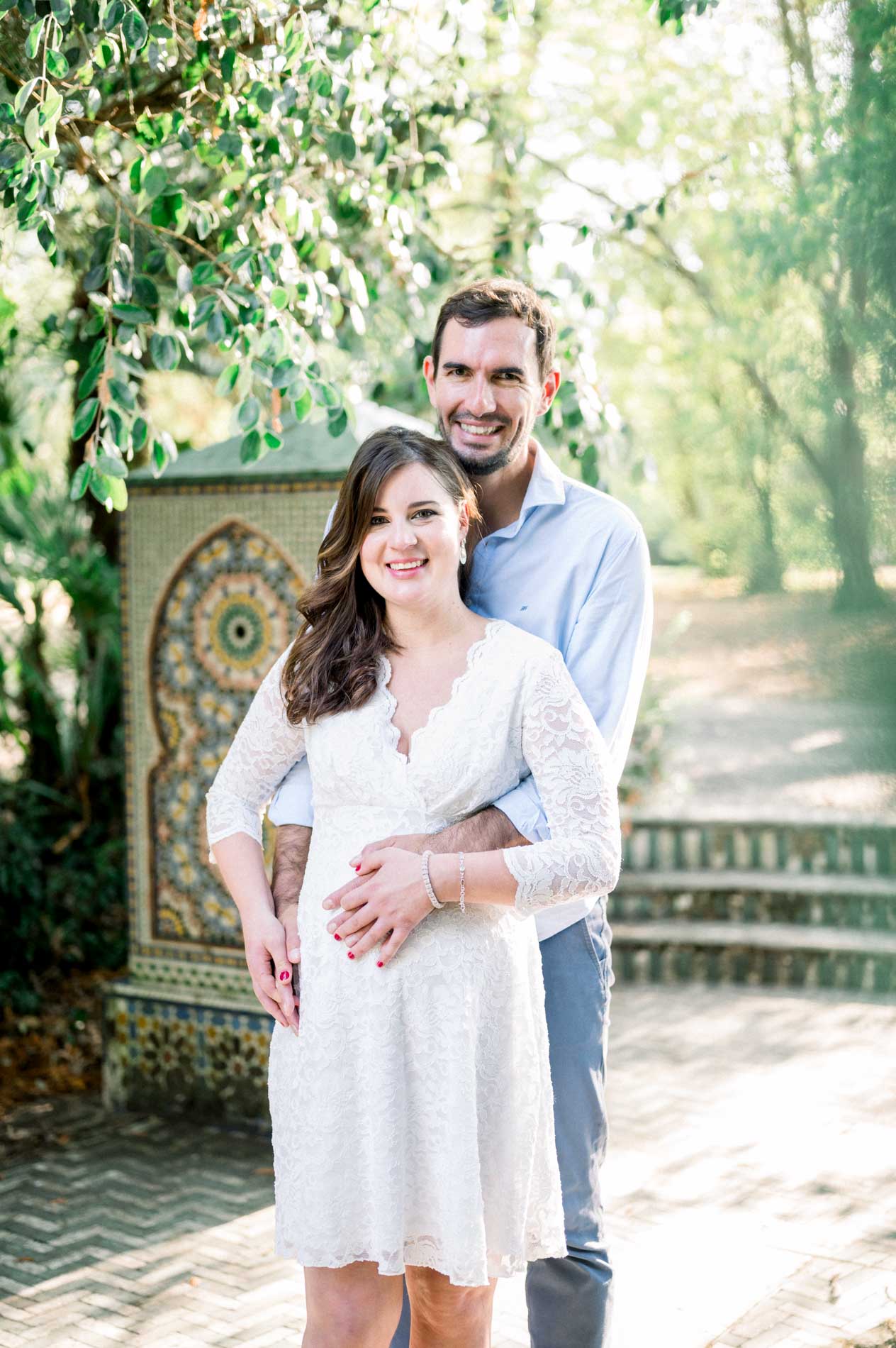 Father-to-be hugging his pregnant partner in front of a mosaic fountain
