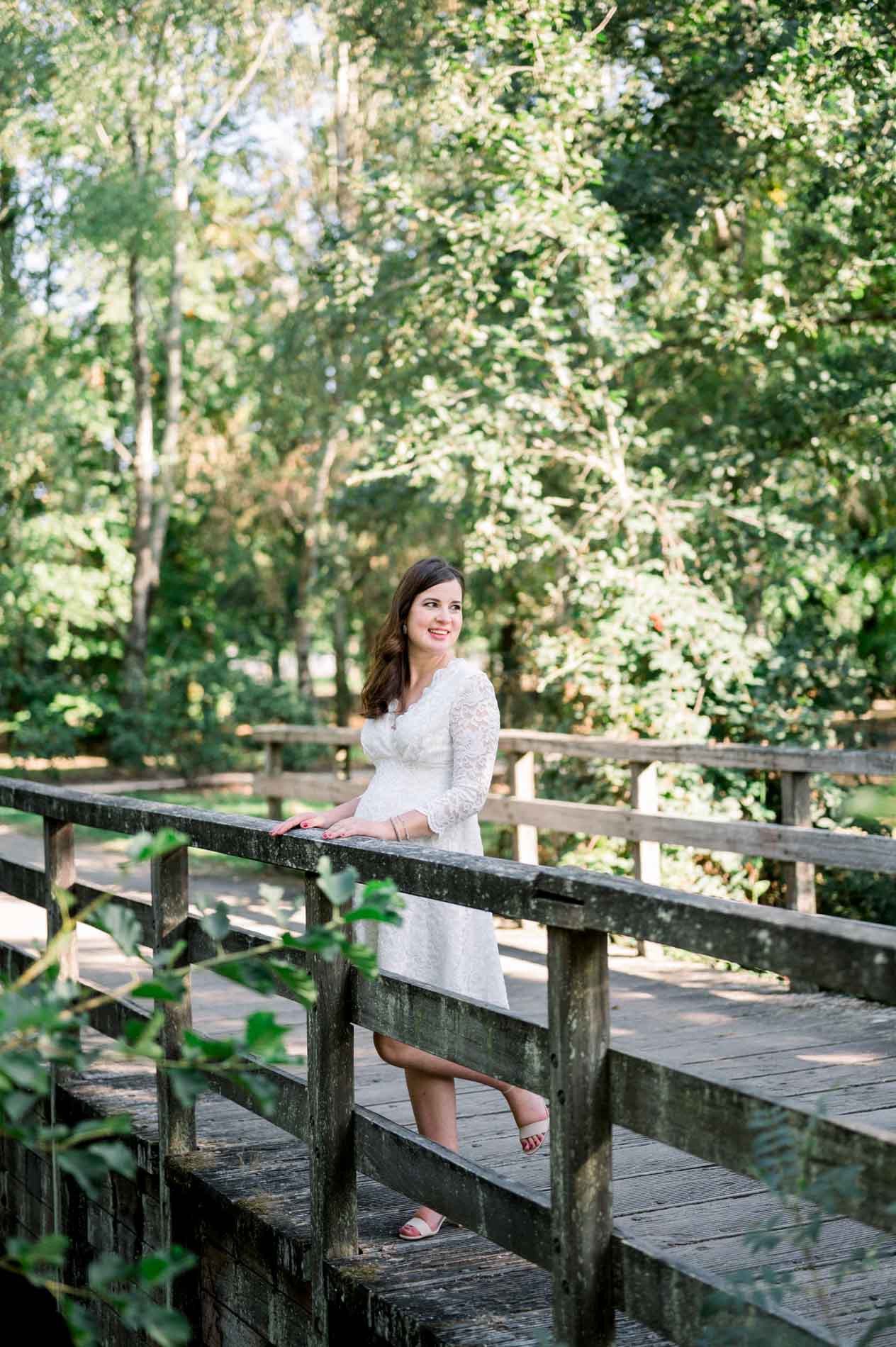 Mother-to-be leaning on the railing of a wooden footbridge