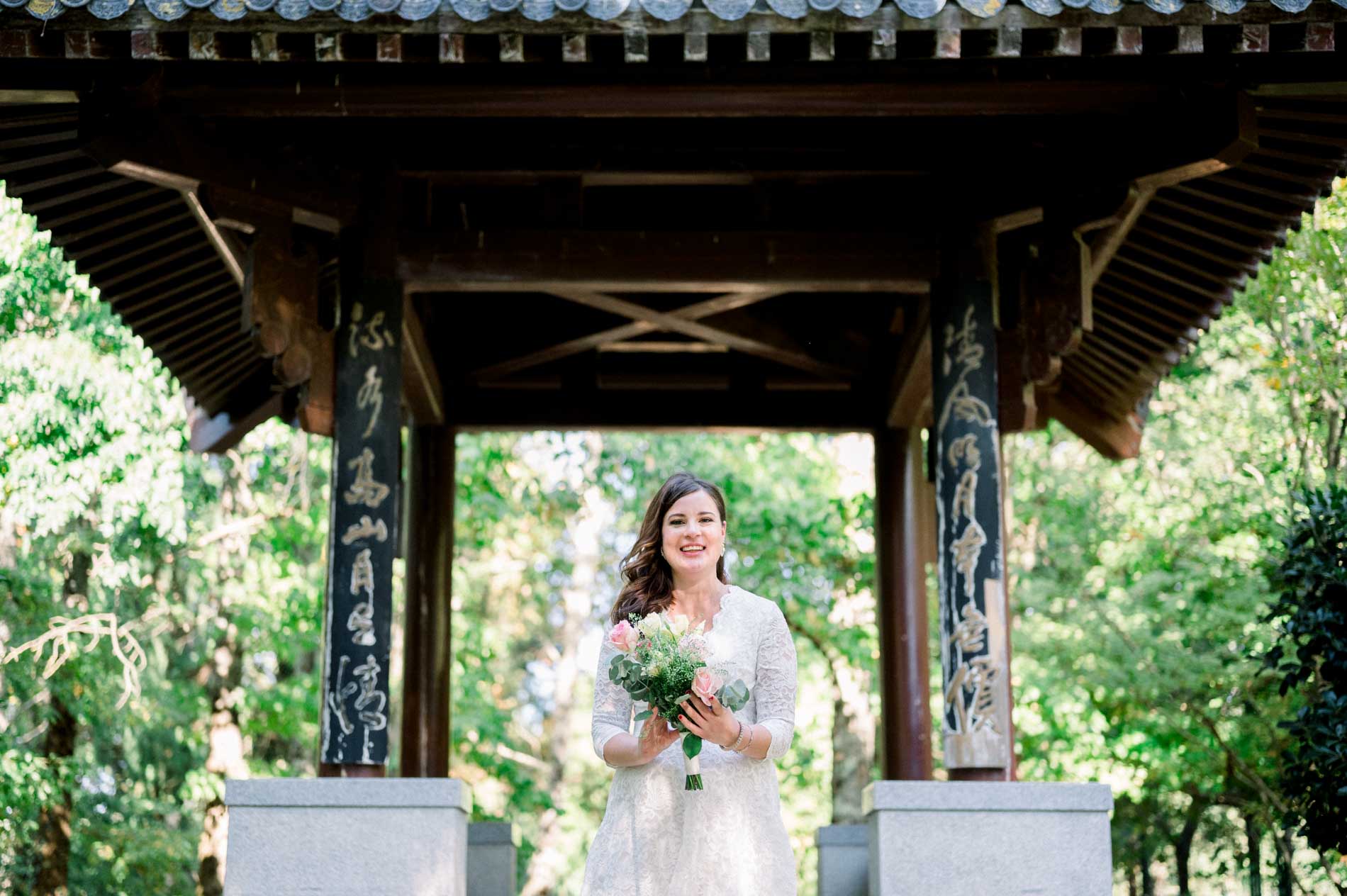 Mother-to-be beneath a wooden Asian-style pavilion, bouquet in hand