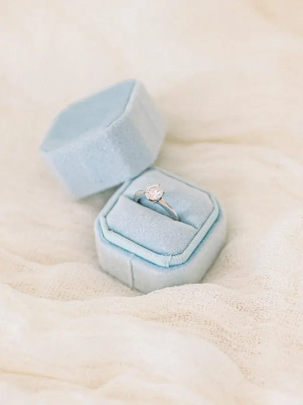 Engagement ring in a pale blue velvet box resting on soft fabric