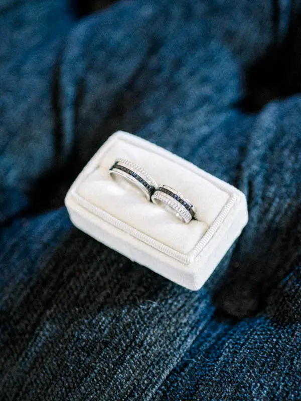 Wedding bands in a white ring box set on a blue tweed jacket