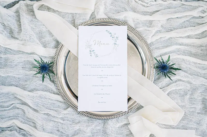 Wedding menu on a silver charger with blue thistles and a silk ribbon