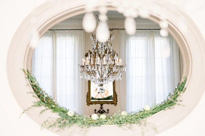 Château salon with a crystal chandelier framed by a foliage-wrapped oval window