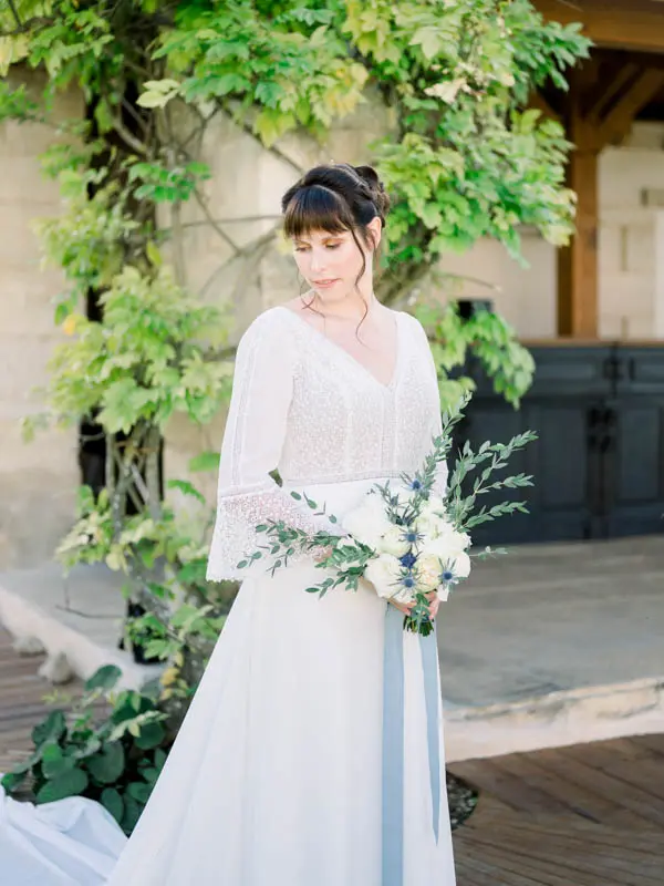 Bride looking down at her white bouquet under the wisteria at Château de Garde