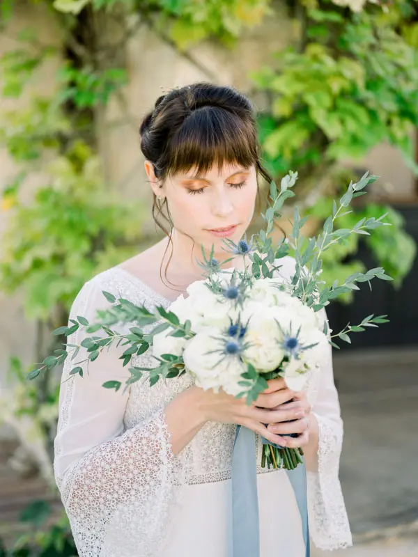 Bride with lowered eyes holding a bouquet of white flowers and thistles