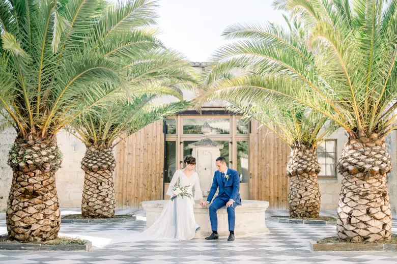 Bride and groom sitting in the palm-lined courtyard of Château de Garde