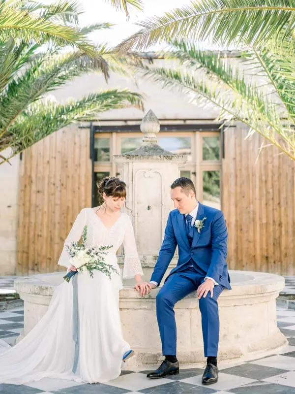 Bride and groom sitting hand in hand on the rim of a stone fountain