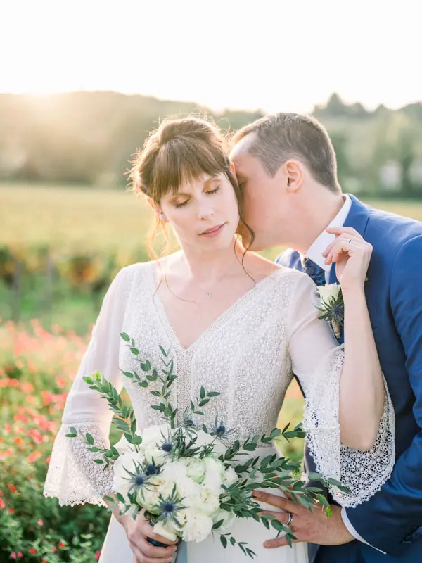 Groom kissing the bride's temple among the vines at sunset