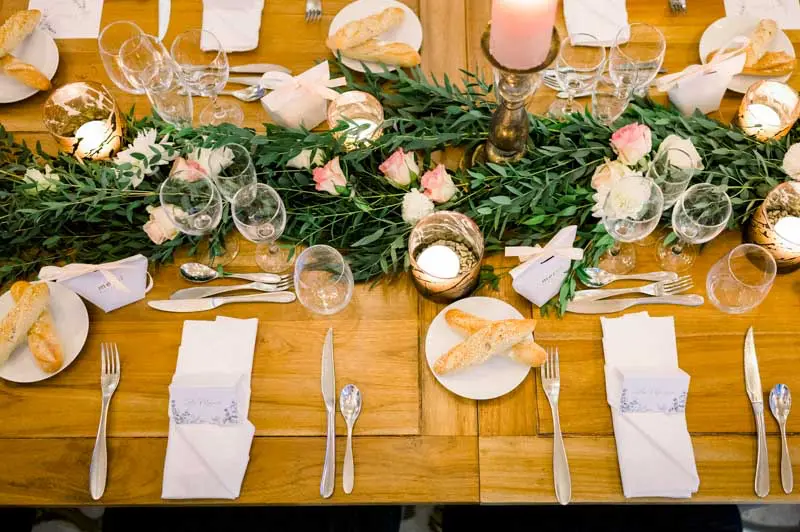Table centrepiece of eucalyptus, roses and gold votives seen from above