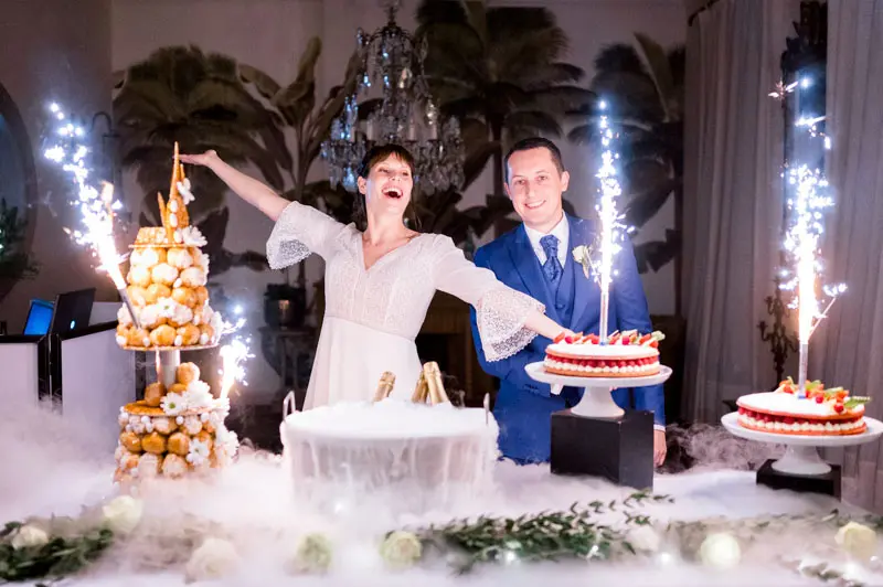 Bride and groom by the croquembouche and cakes lit with sparklers