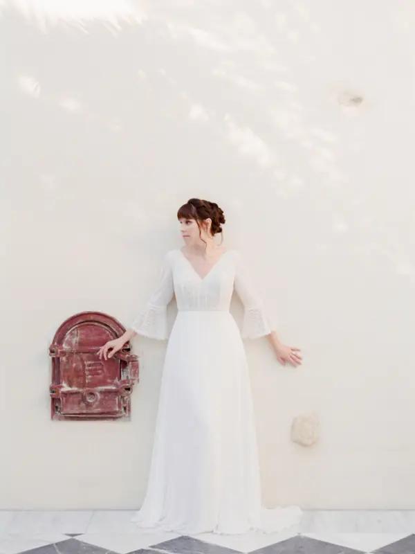 Bride in a bell-sleeved gown against a white wall beside an old oven door