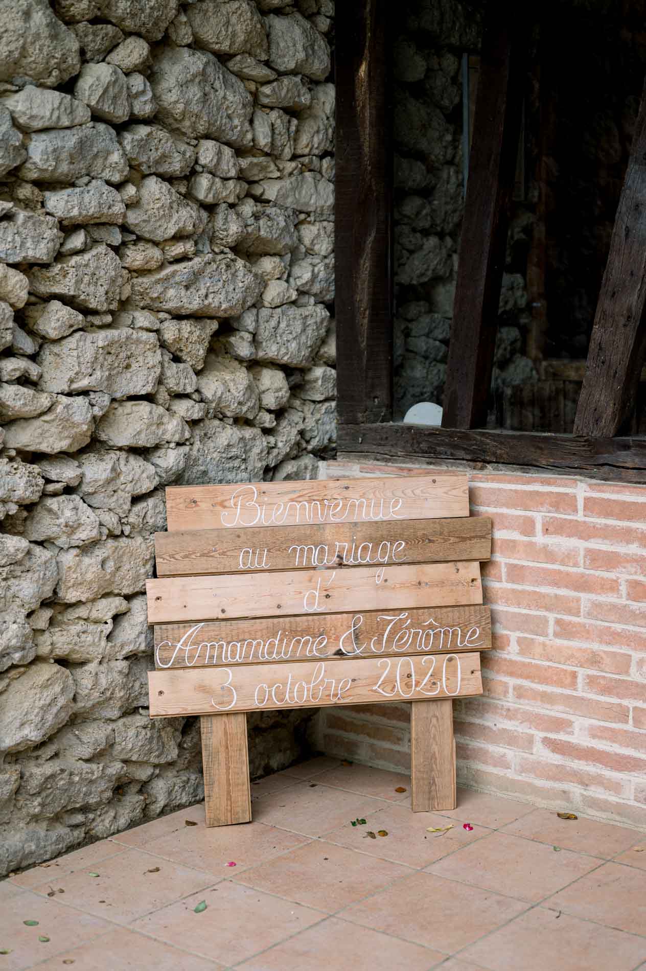 Welcome sign made of wooden planks resting against a stone wall