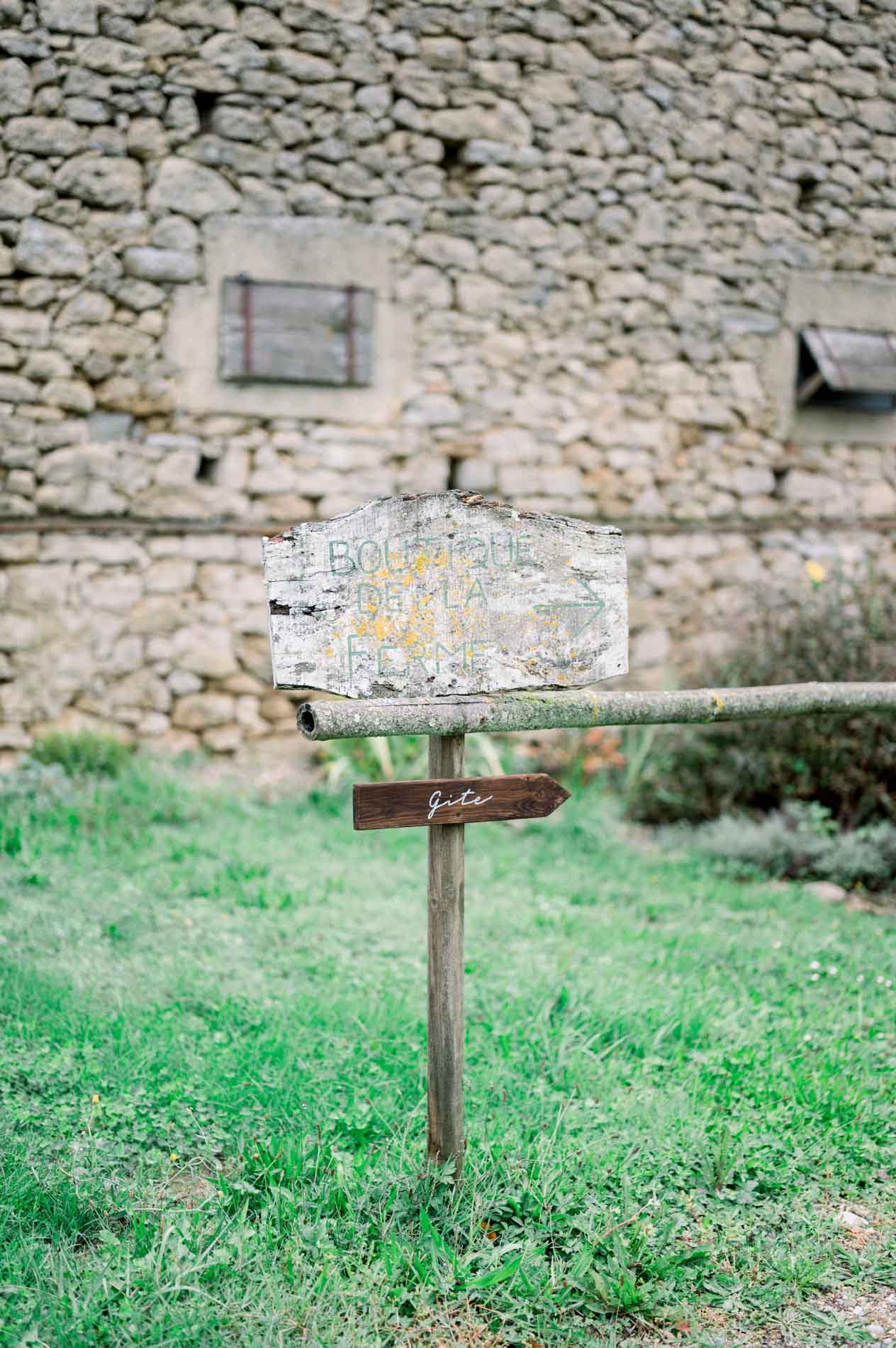 Small wooden sign set in the grass before a stone wall