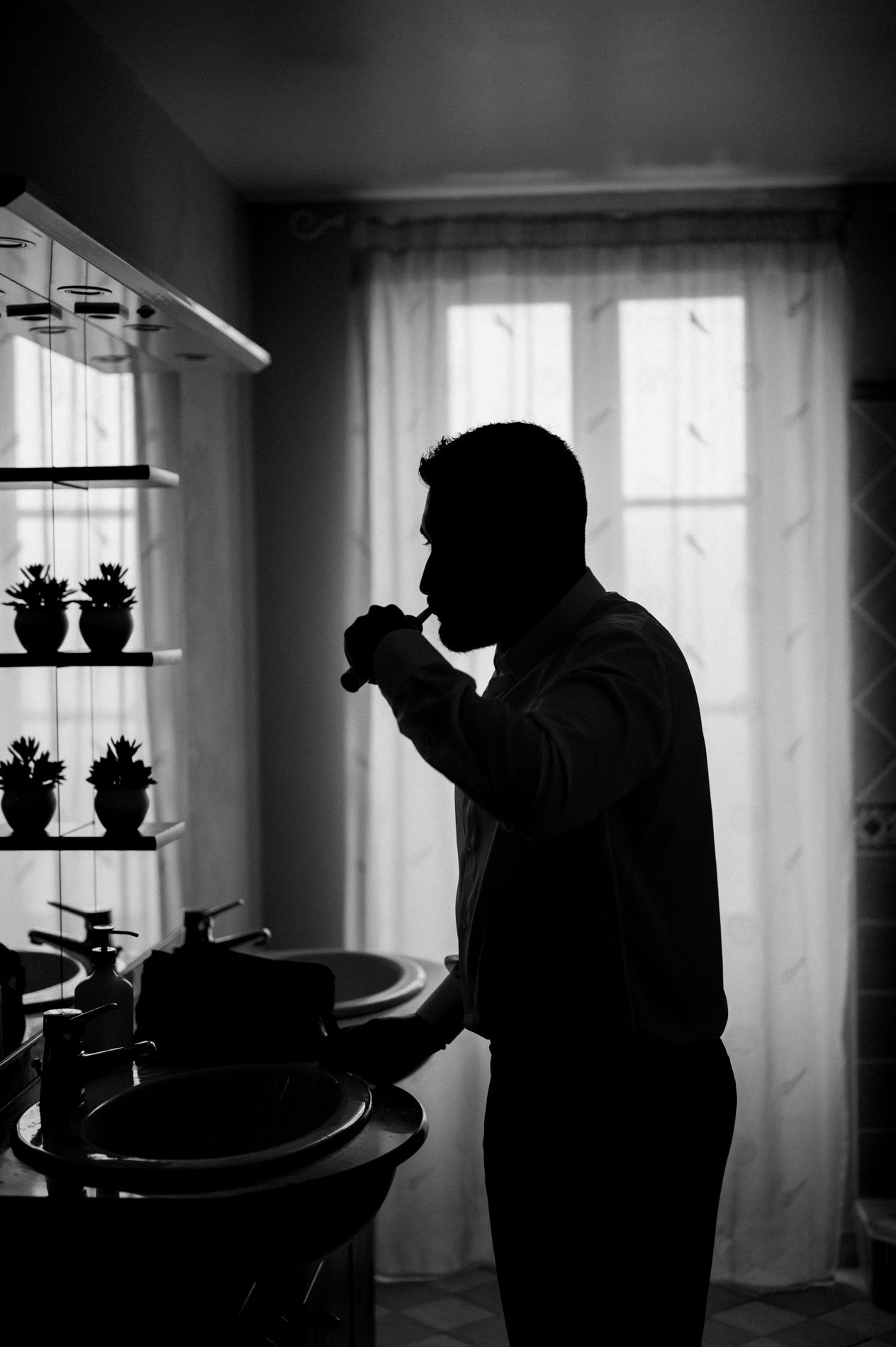 Silhouette of the groom brushing his teeth by the window, in black and white