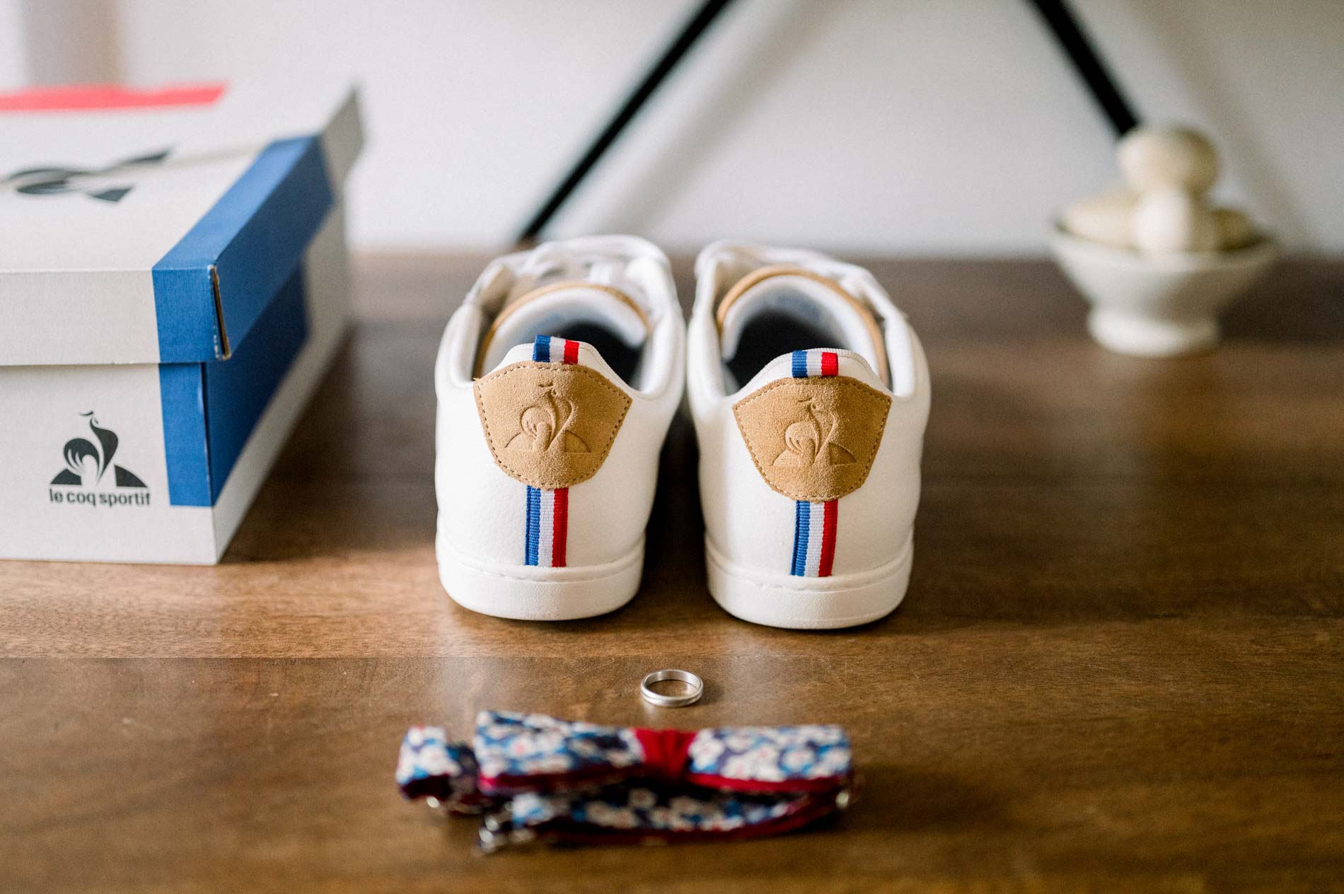 Groom's white sneakers, wedding ring and bow tie on a wooden table