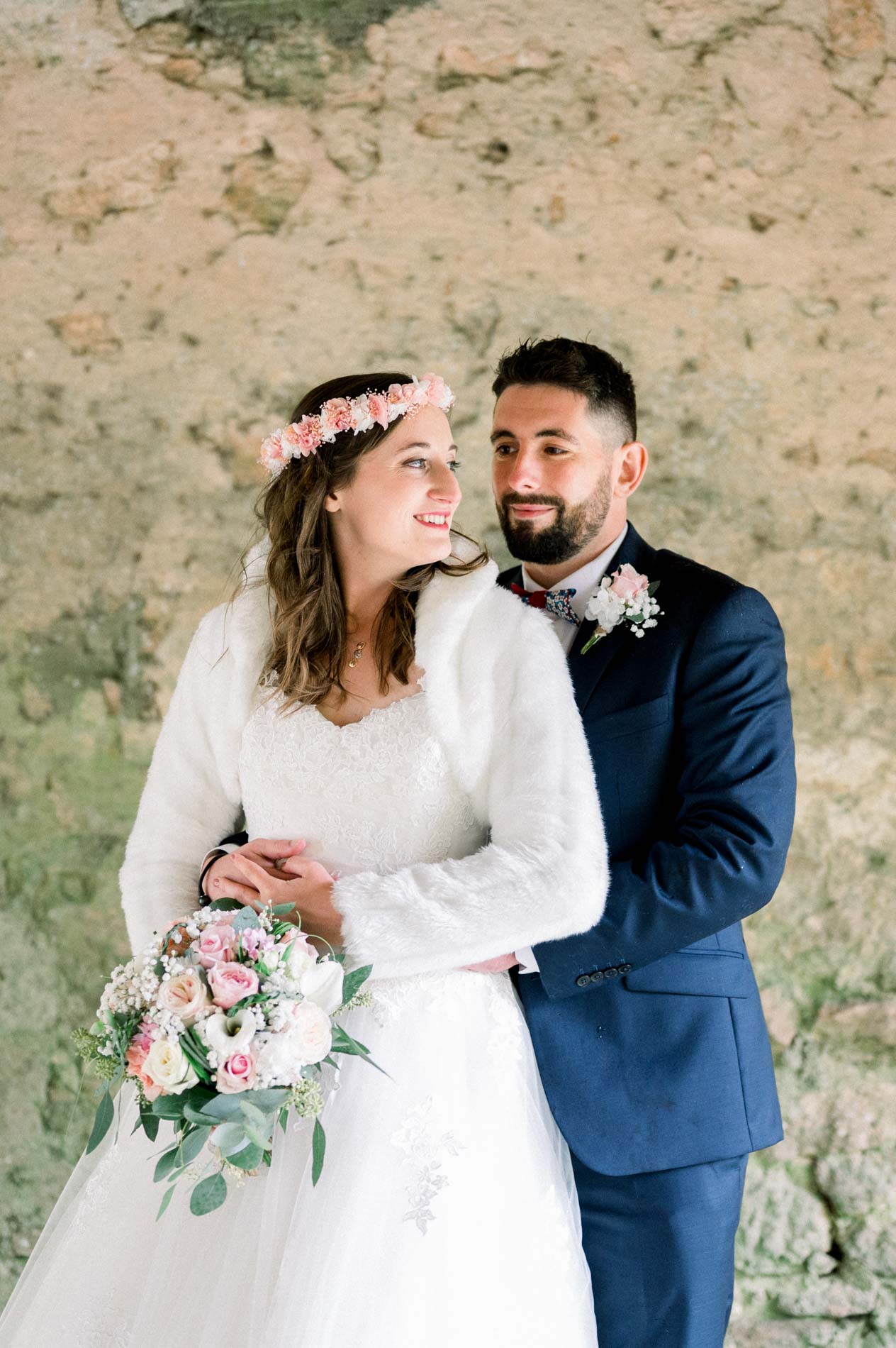 Bride and groom embracing and gazing at each other by an ochre farm wall