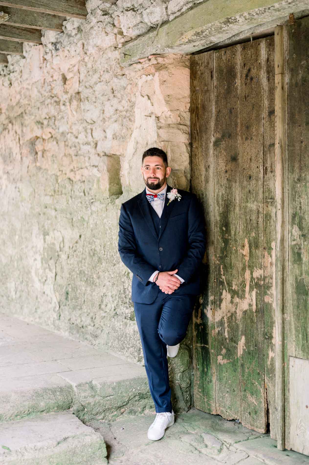 Groom leaning against an old wooden barn door
