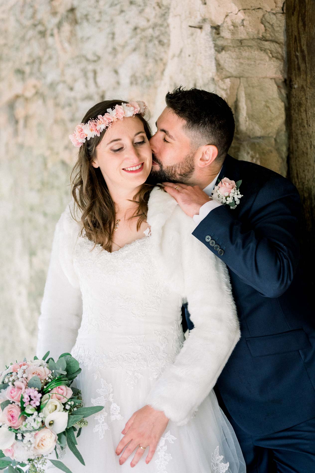 Groom kissing the bride's cheek in front of a stone wall