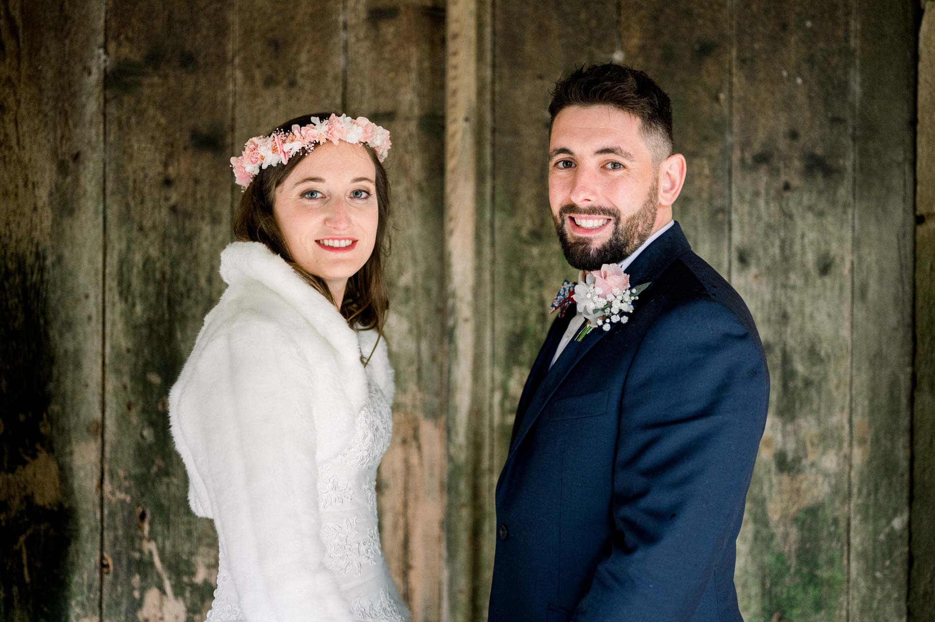 Smiling bride and groom side by side before an old wooden gate