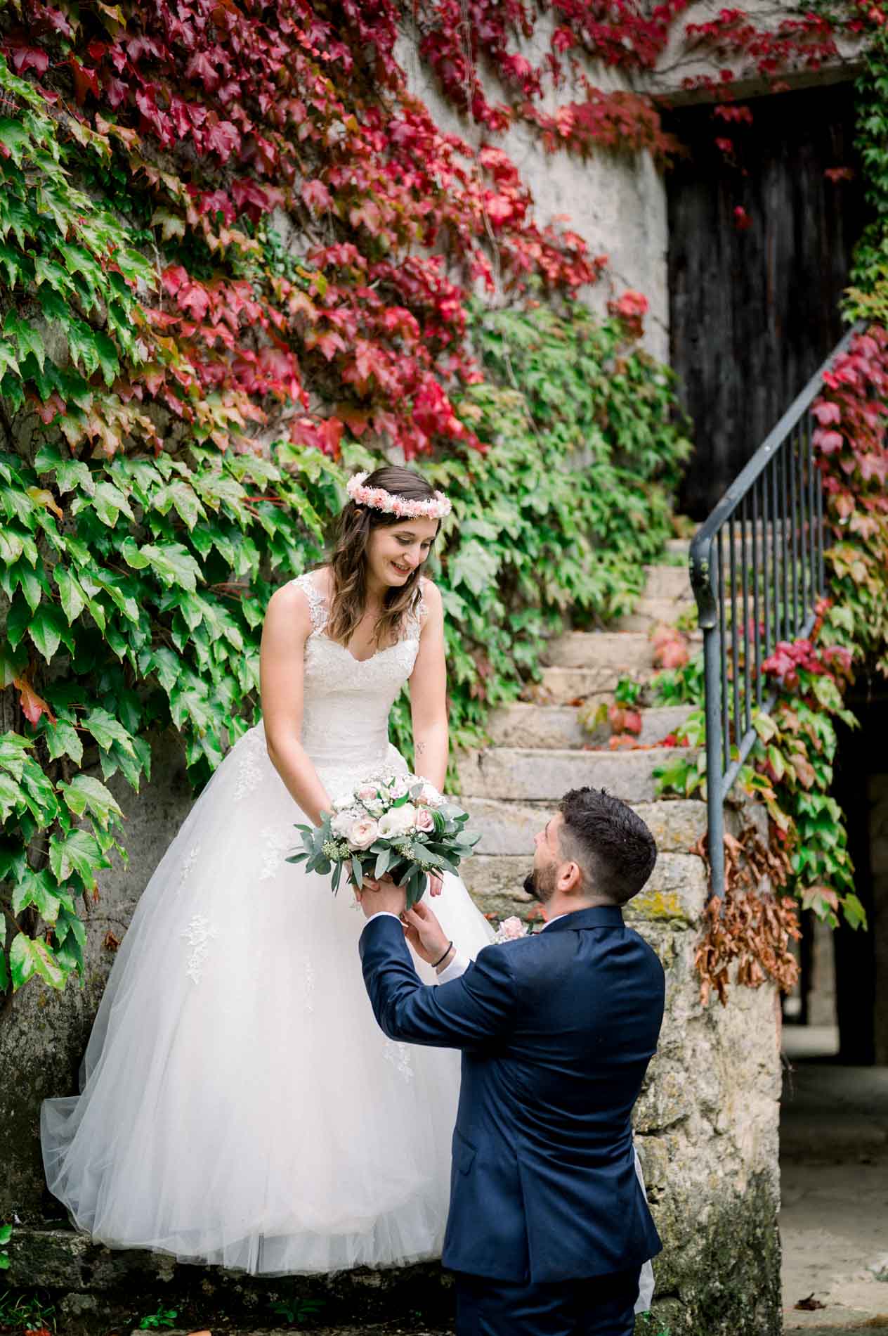 Groom kneeling before the bride at the foot of a leafy stone stairway