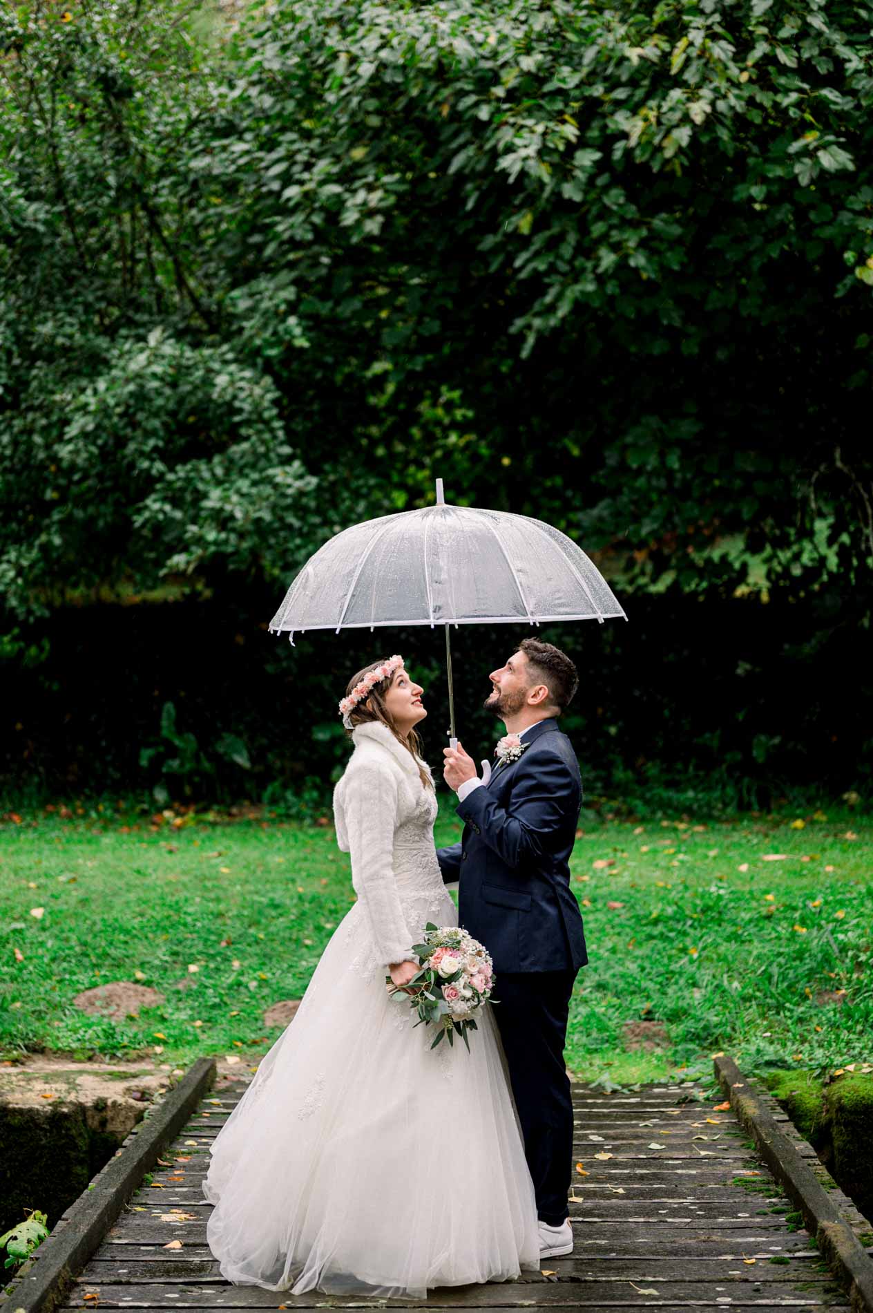 Bride and groom face to face under an umbrella on a small wooden bridge