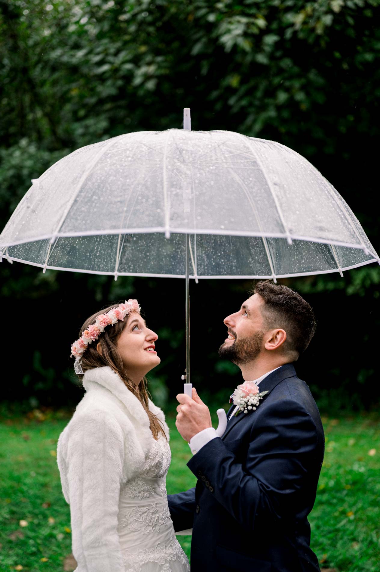 Smiling bride and groom under a clear umbrella in the garden