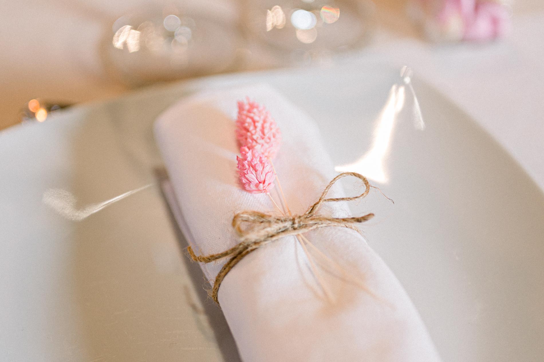 Napkin tied with twine and a small pink favour on a plate