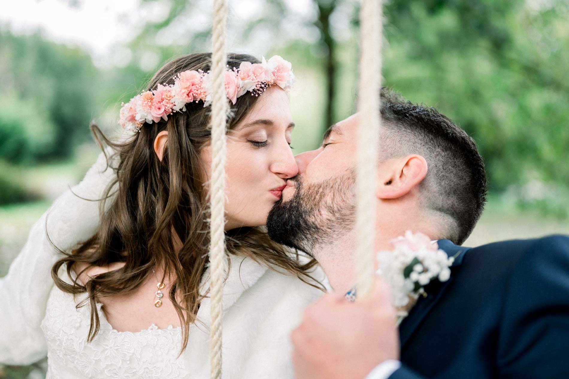 Bride and groom kissing between the ropes of a swing