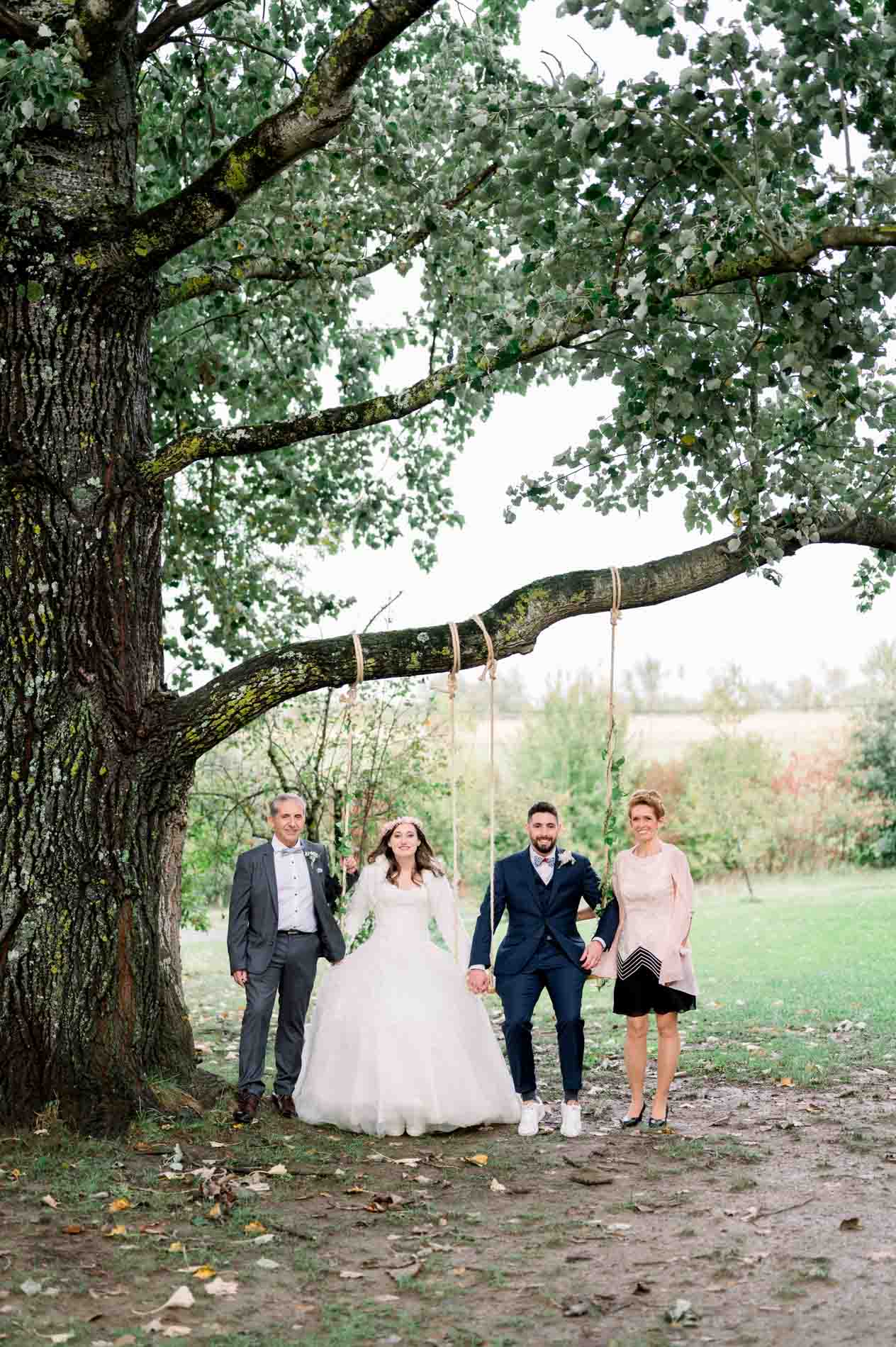 Bride, groom and two guests under a large oak in the farm grounds