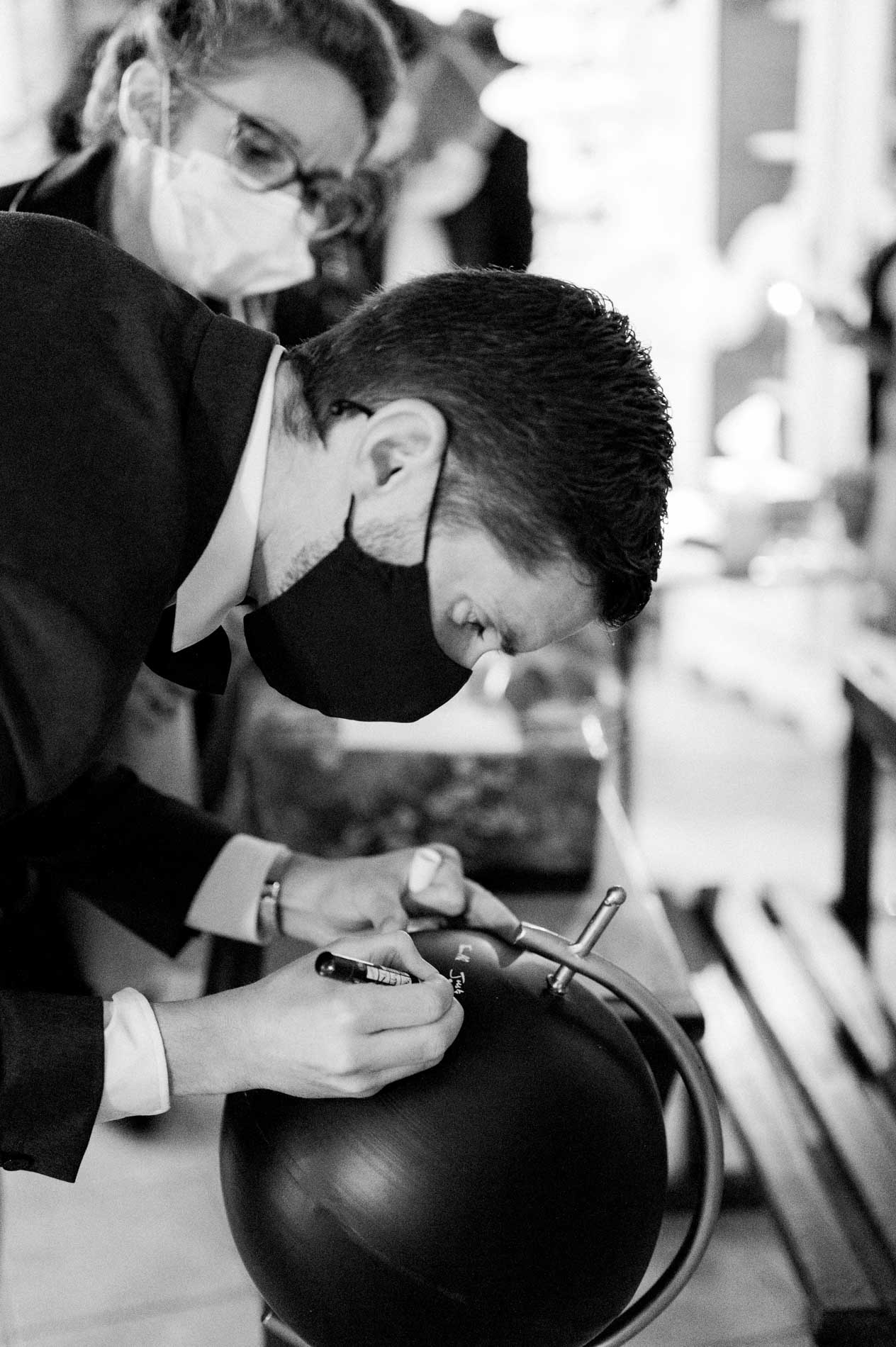 Masked guests writing a message on a black sphere, in black and white