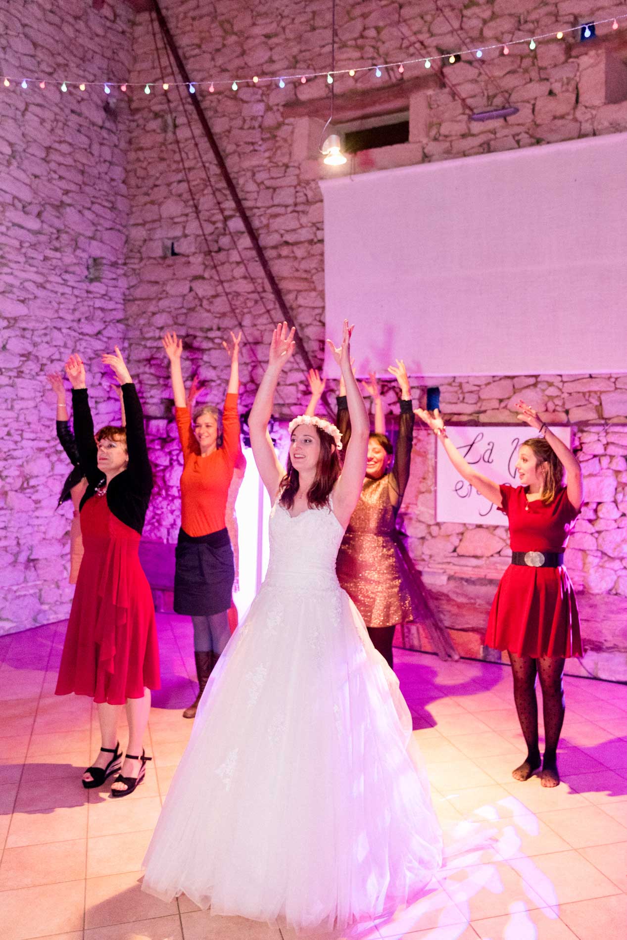 Bride and guests dancing with raised arms under pink lights