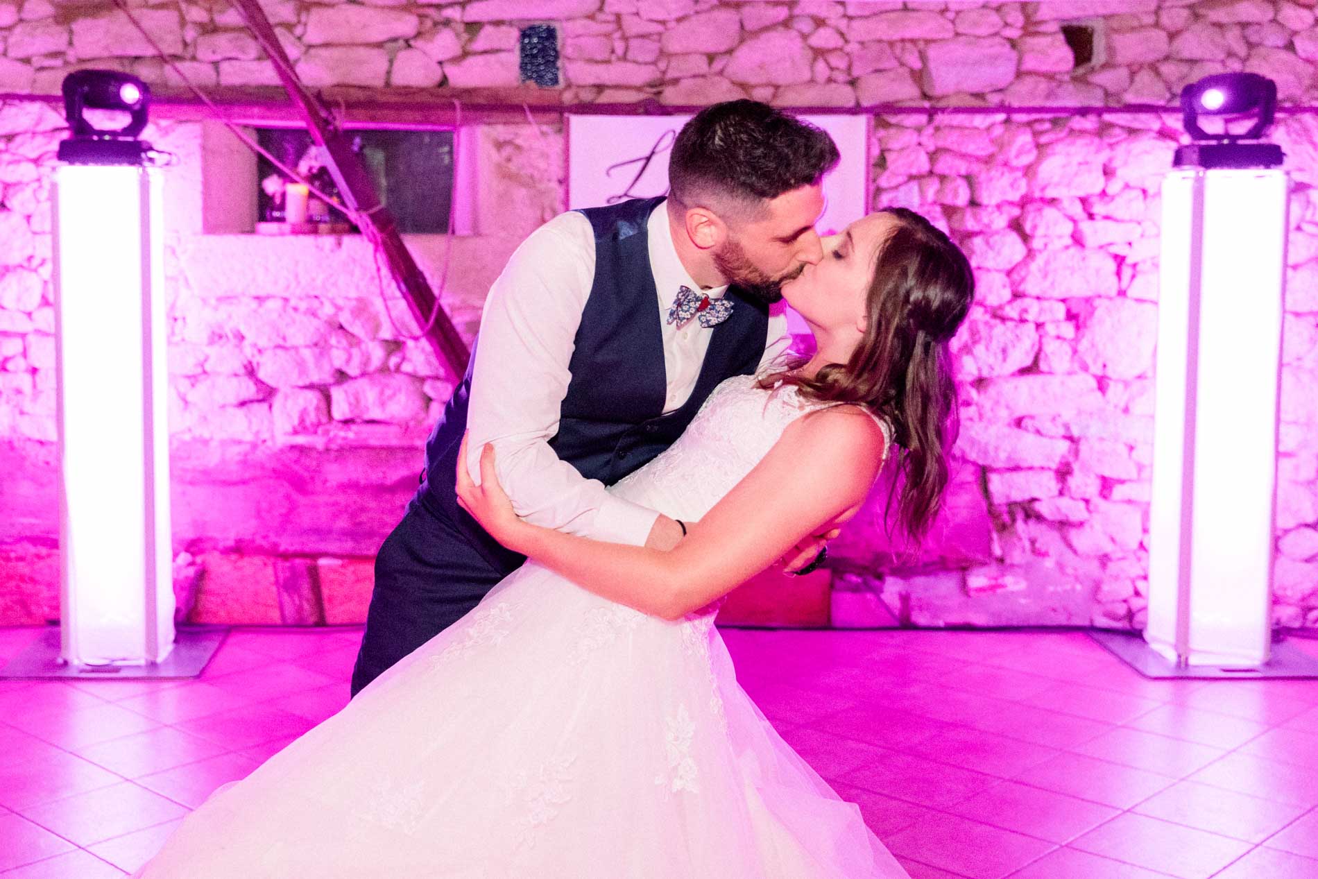 Bride and groom kissing during their first dance under pink lights