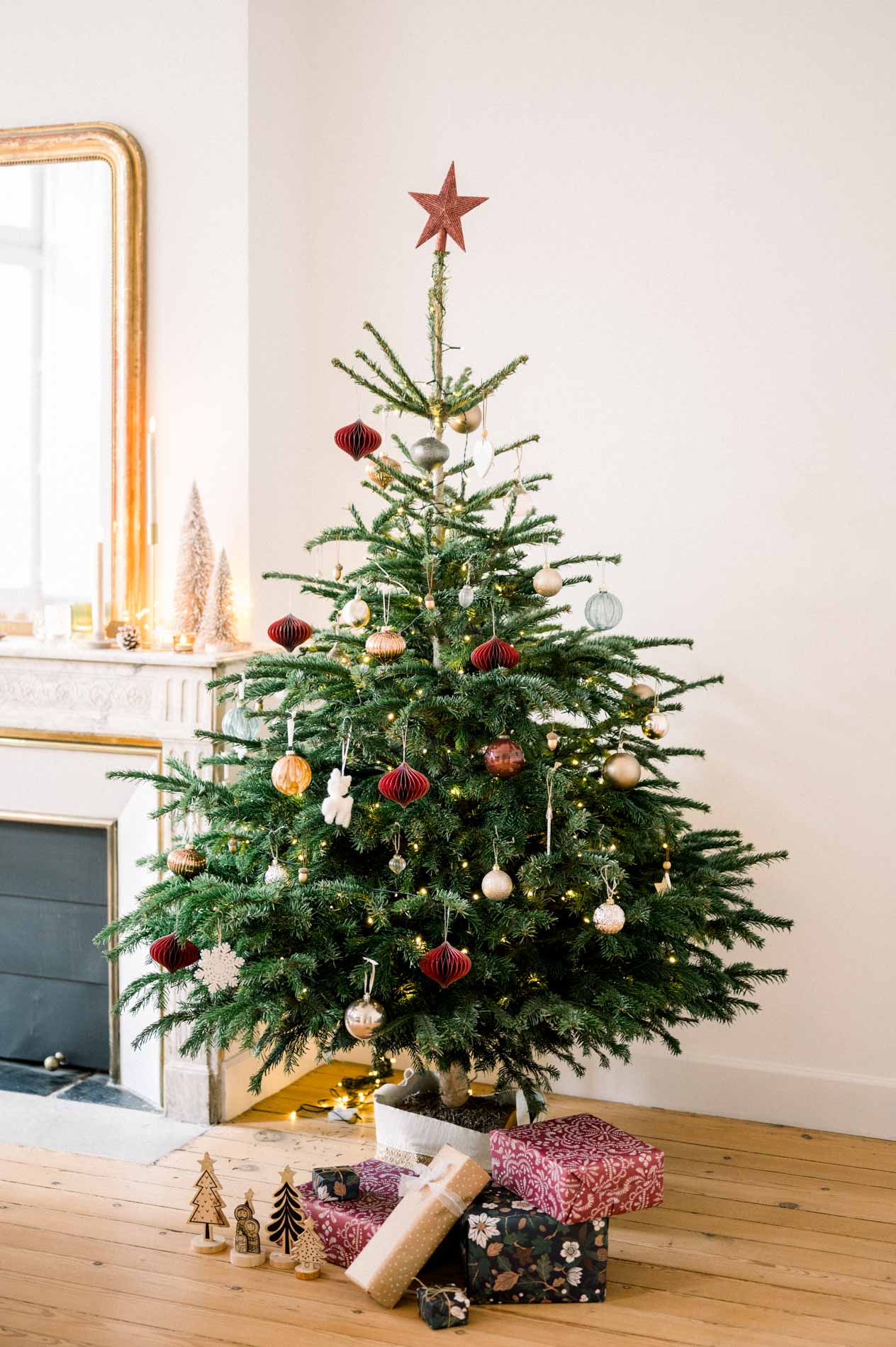 Decorated Christmas tree in front of a marble fireplace and gilded mirror