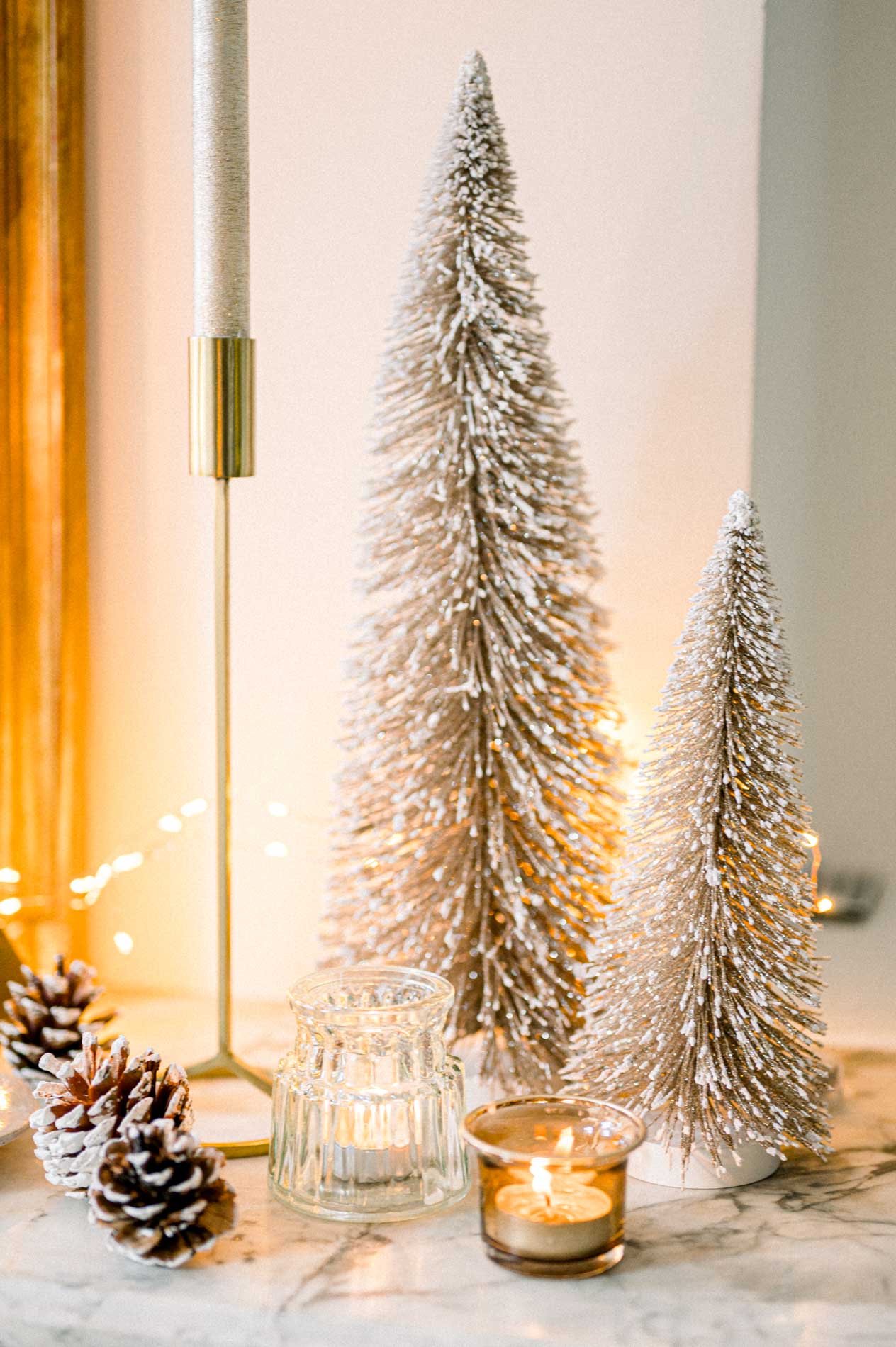 Small snowy bottle-brush trees, pine cones and a tealight on the mantelpiece