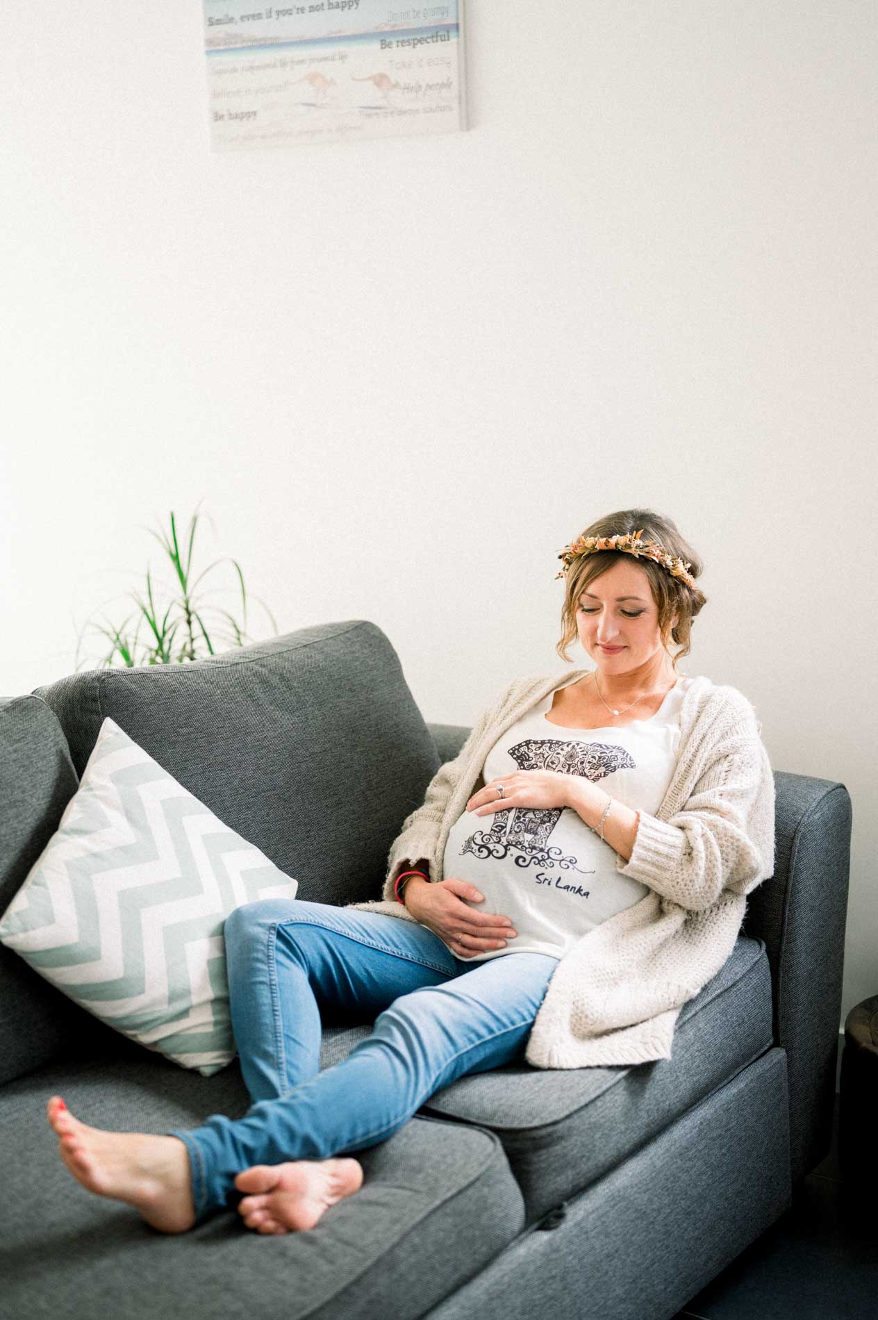 Future maman assise sur le canapé, mains sur le ventre, couronne de fleurs séchées