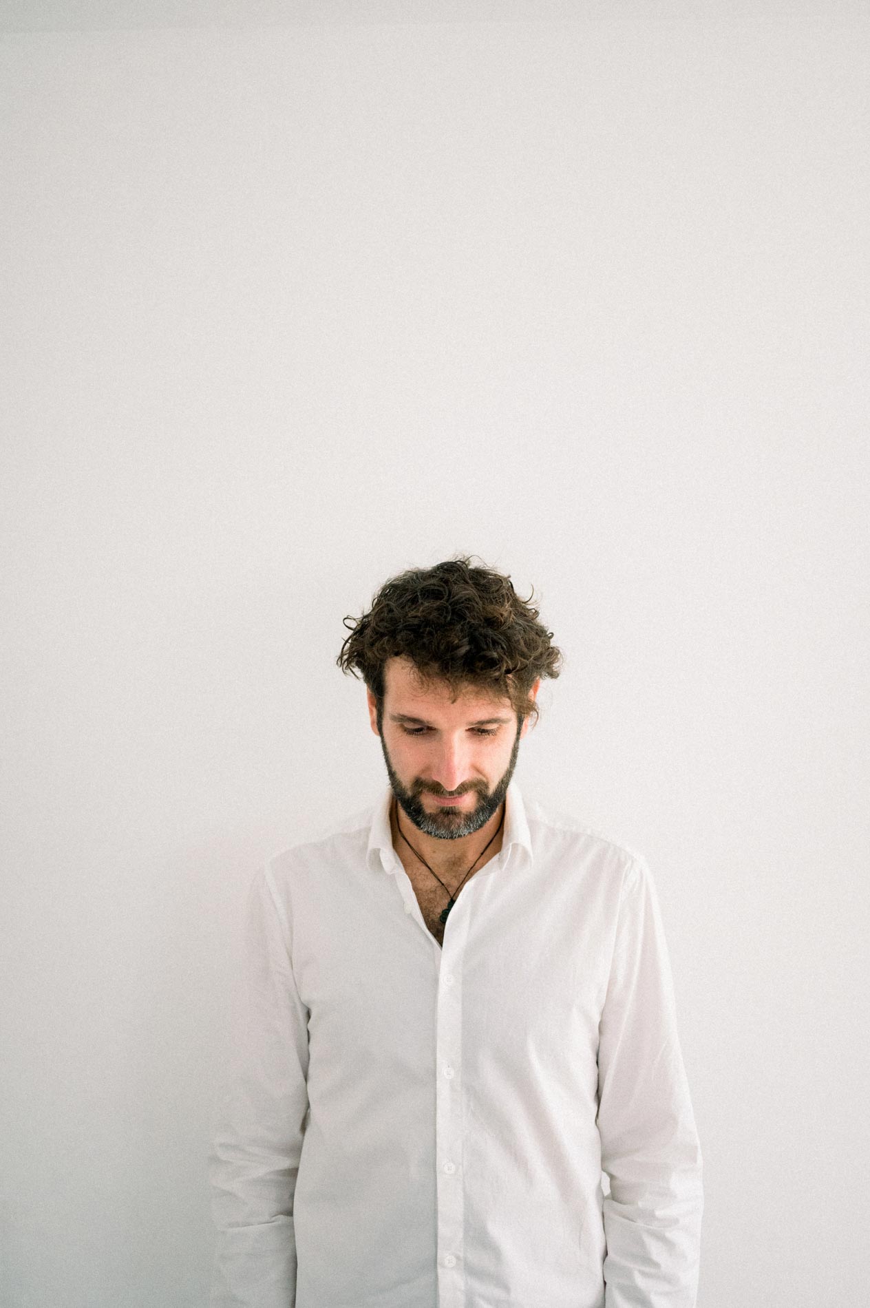 Le futur papa en chemise blanche, regard baissé, devant un mur blanc