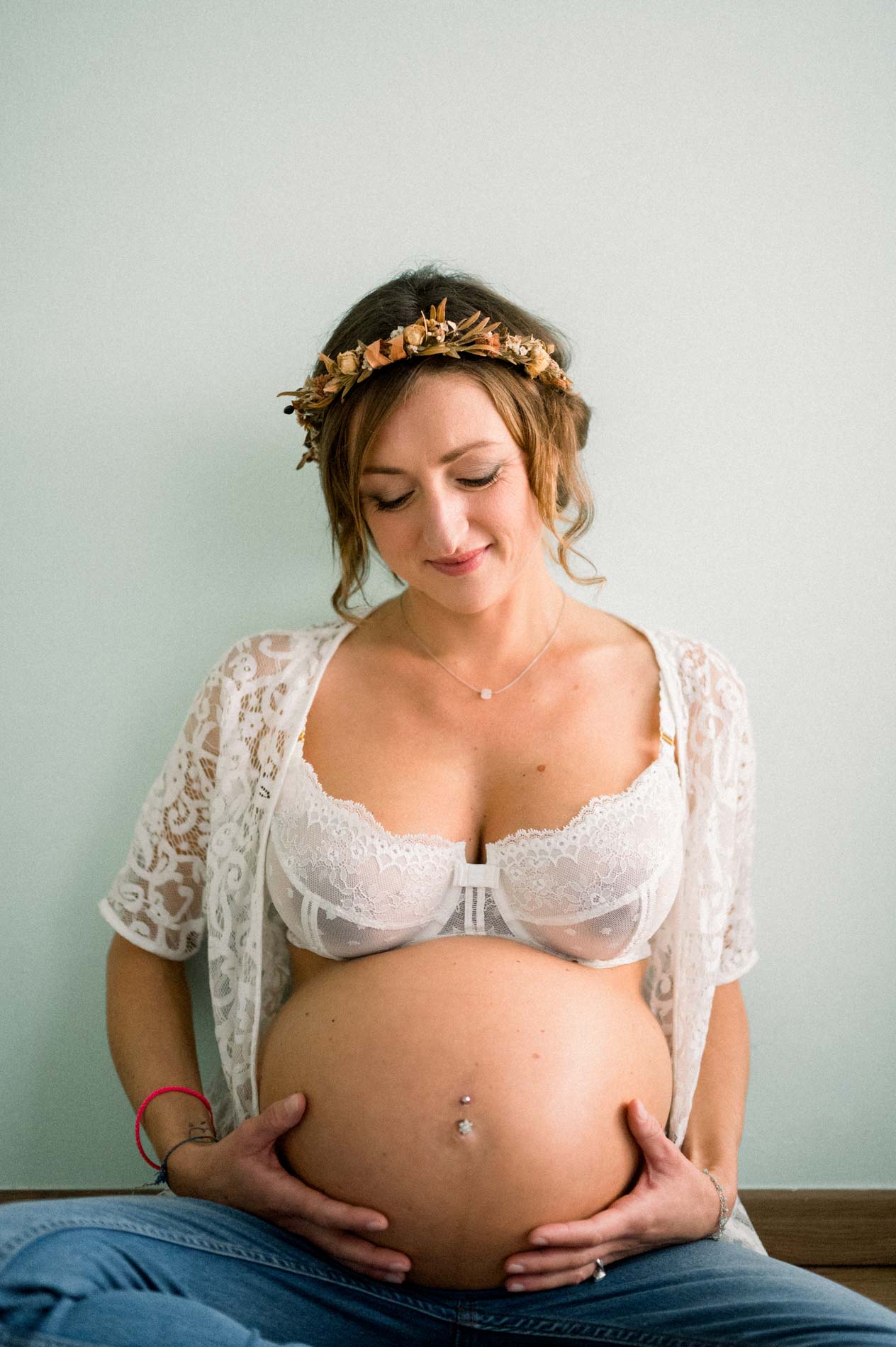 Future maman en dentelle blanche tenant son ventre, yeux baissés