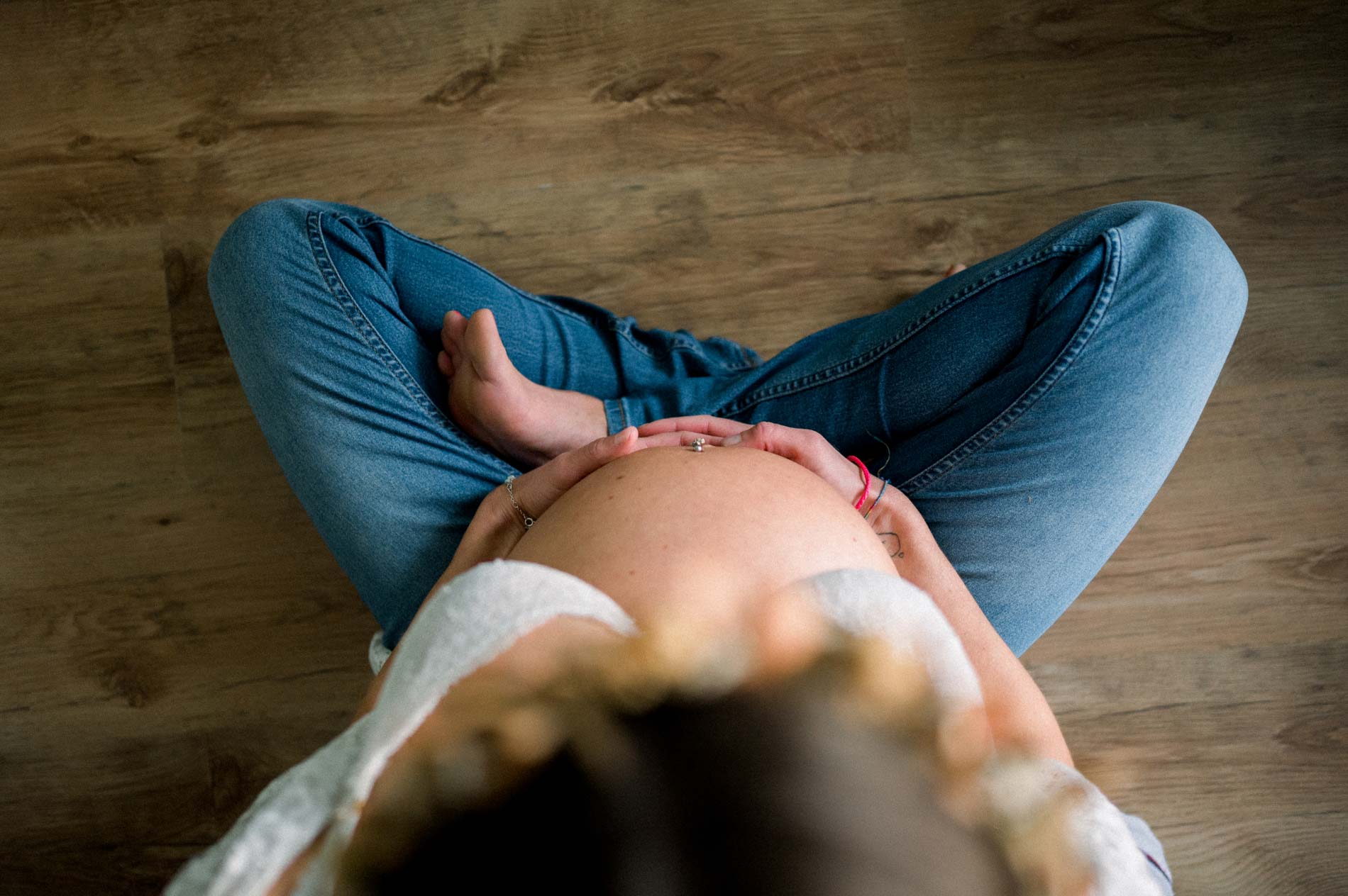Vue de dessus de la future maman assise en tailleur, mains sur le ventre
