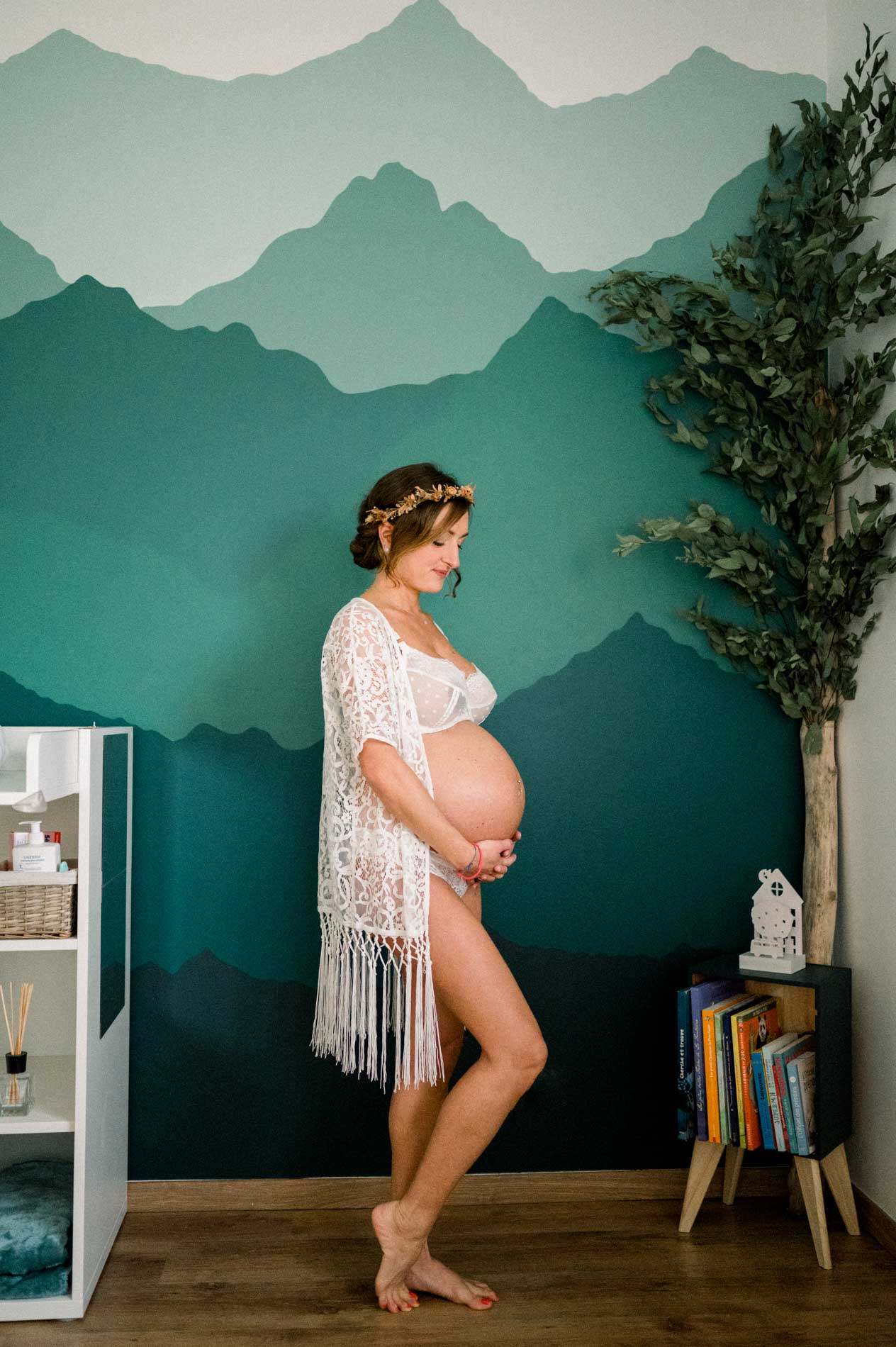 Future maman de profil devant une fresque de montagnes vertes dans la chambre de bébé