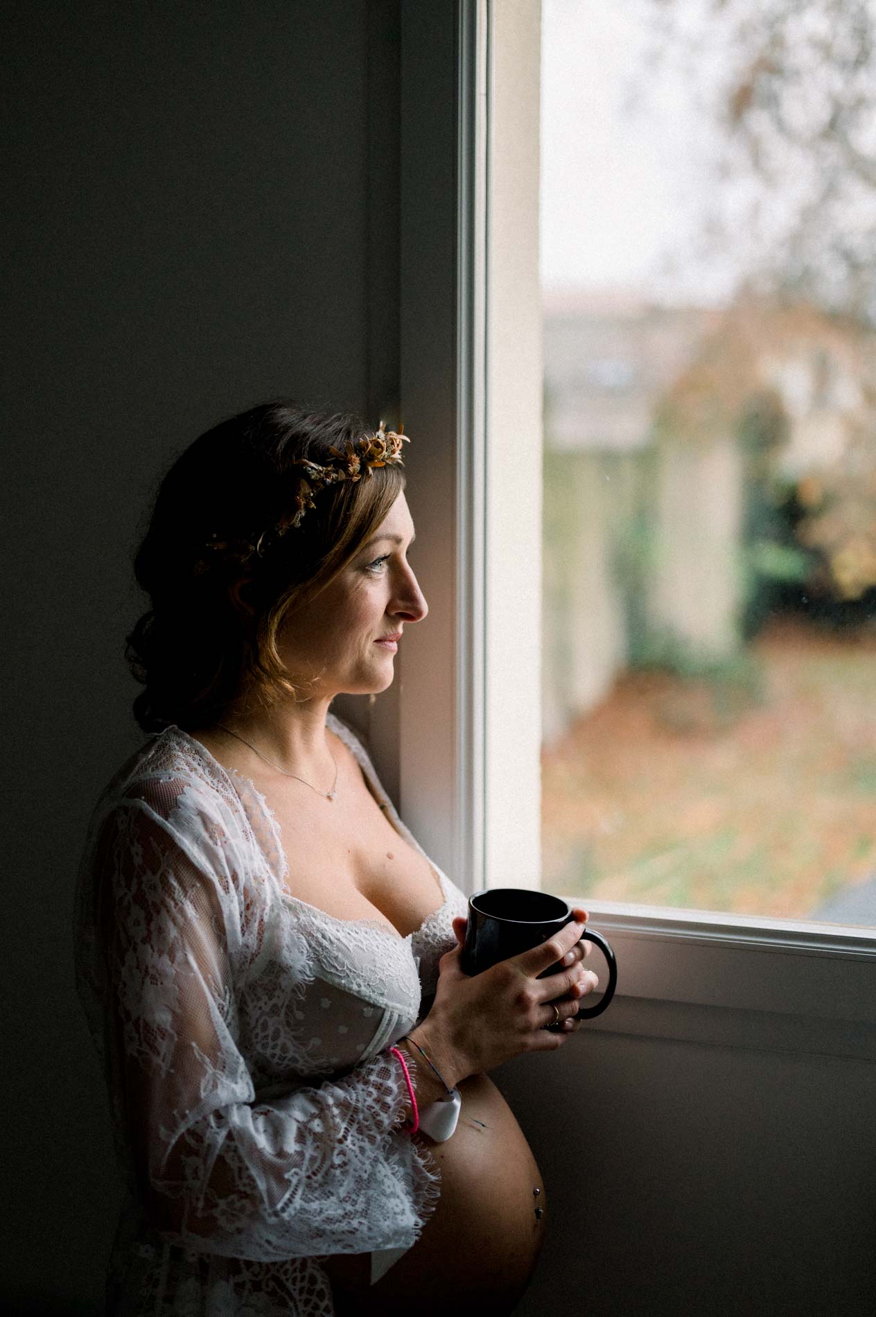 Future maman près de la fenêtre, une tasse à la main, en clair-obscur