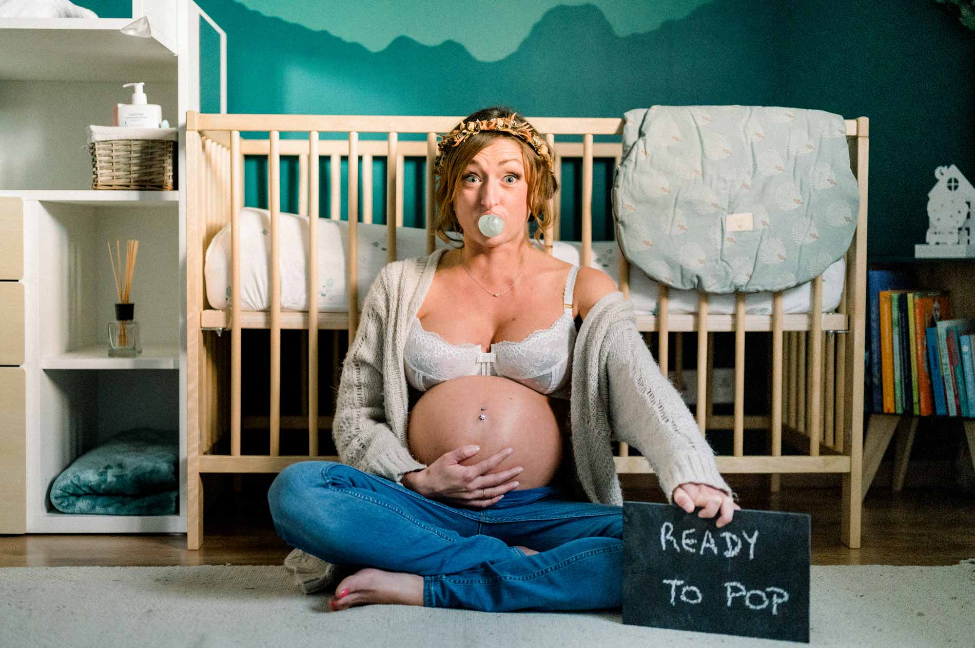Future maman souriante devant le berceau avec son ardoise « Ready to pop »
