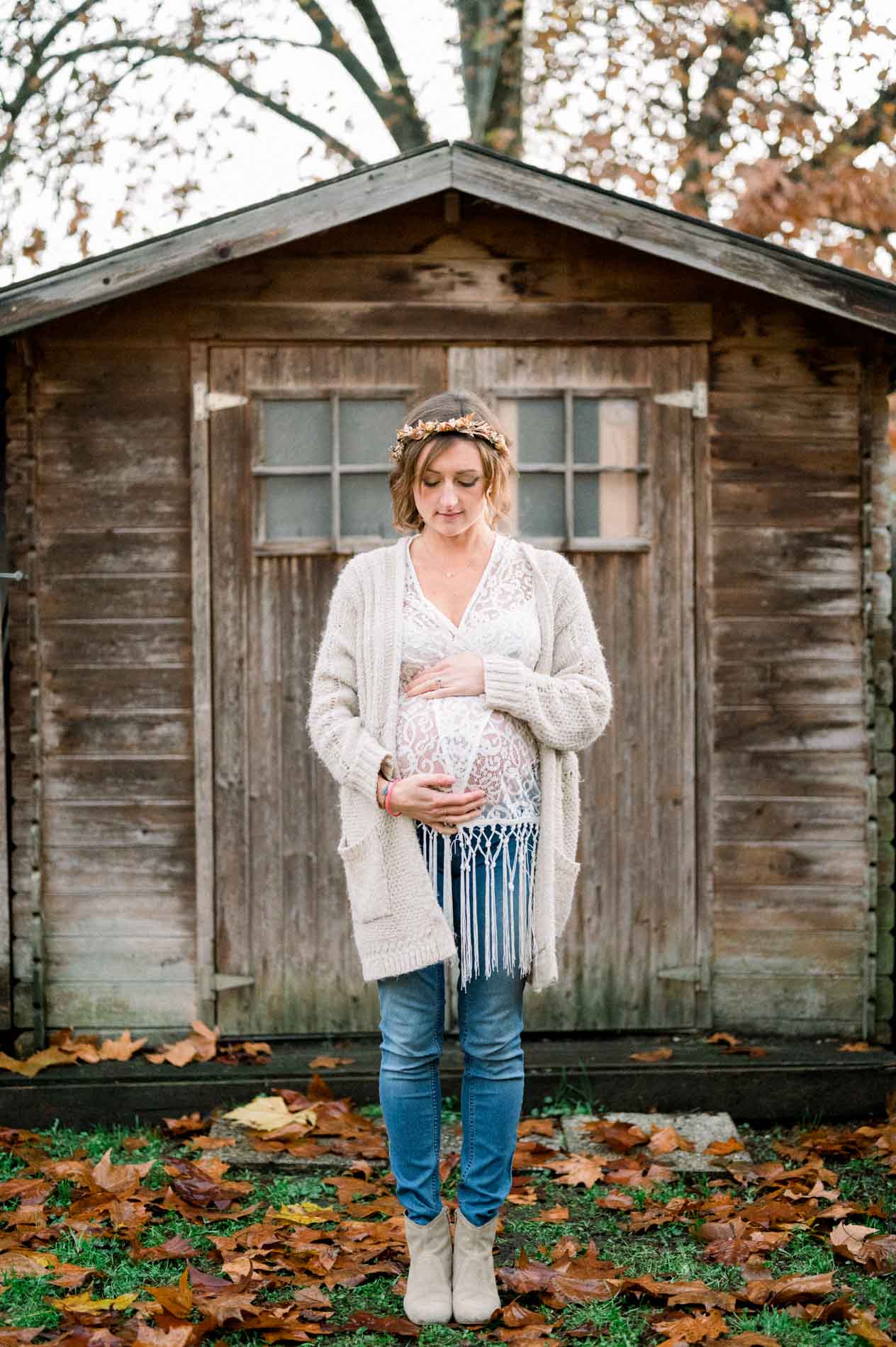 Future maman en gilet devant une cabane en bois en automne
